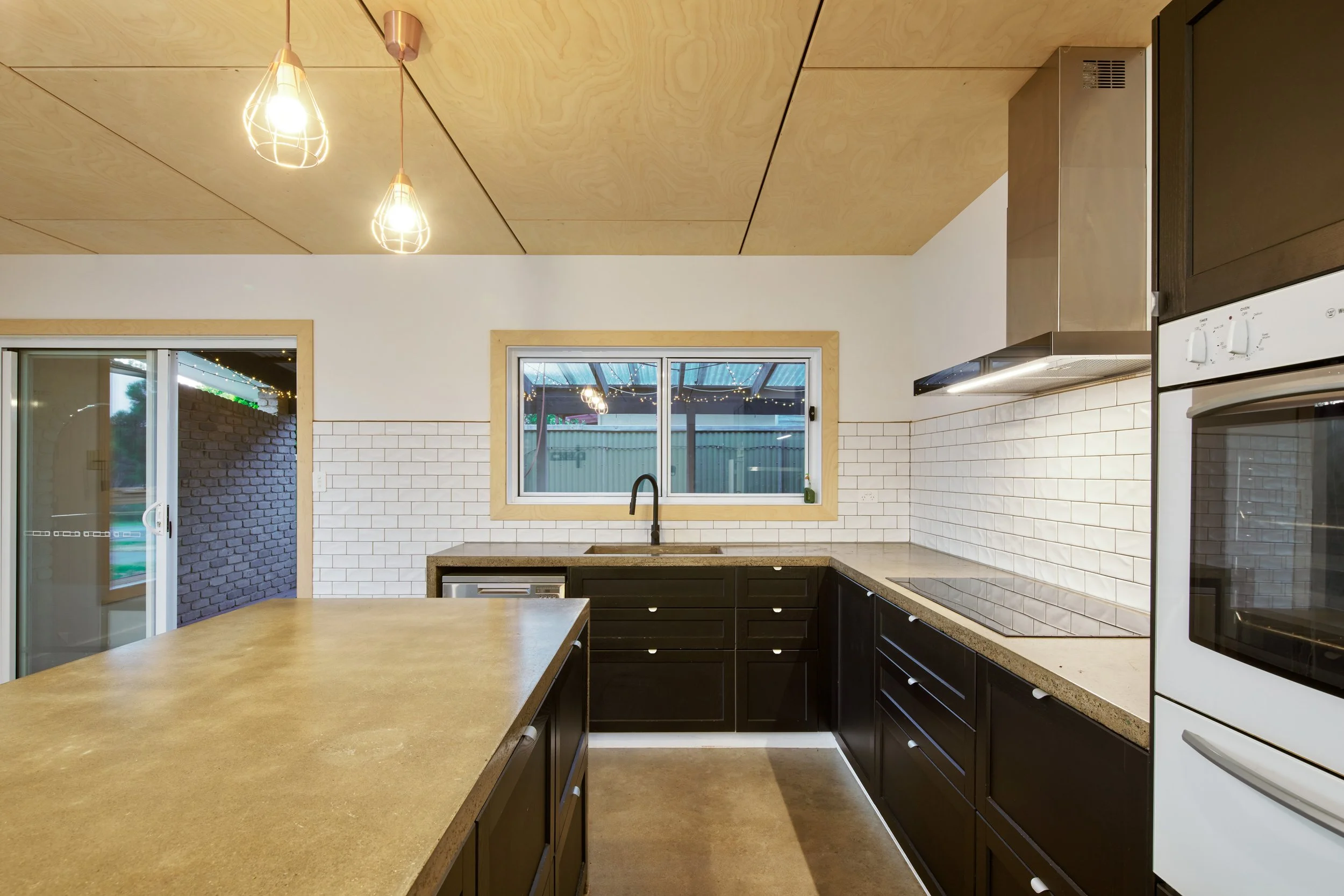 Modern kitchen with black cabinets, white subway tile backsplash, granite countertops, window above the sink, and wooden ceiling with hanging lights.