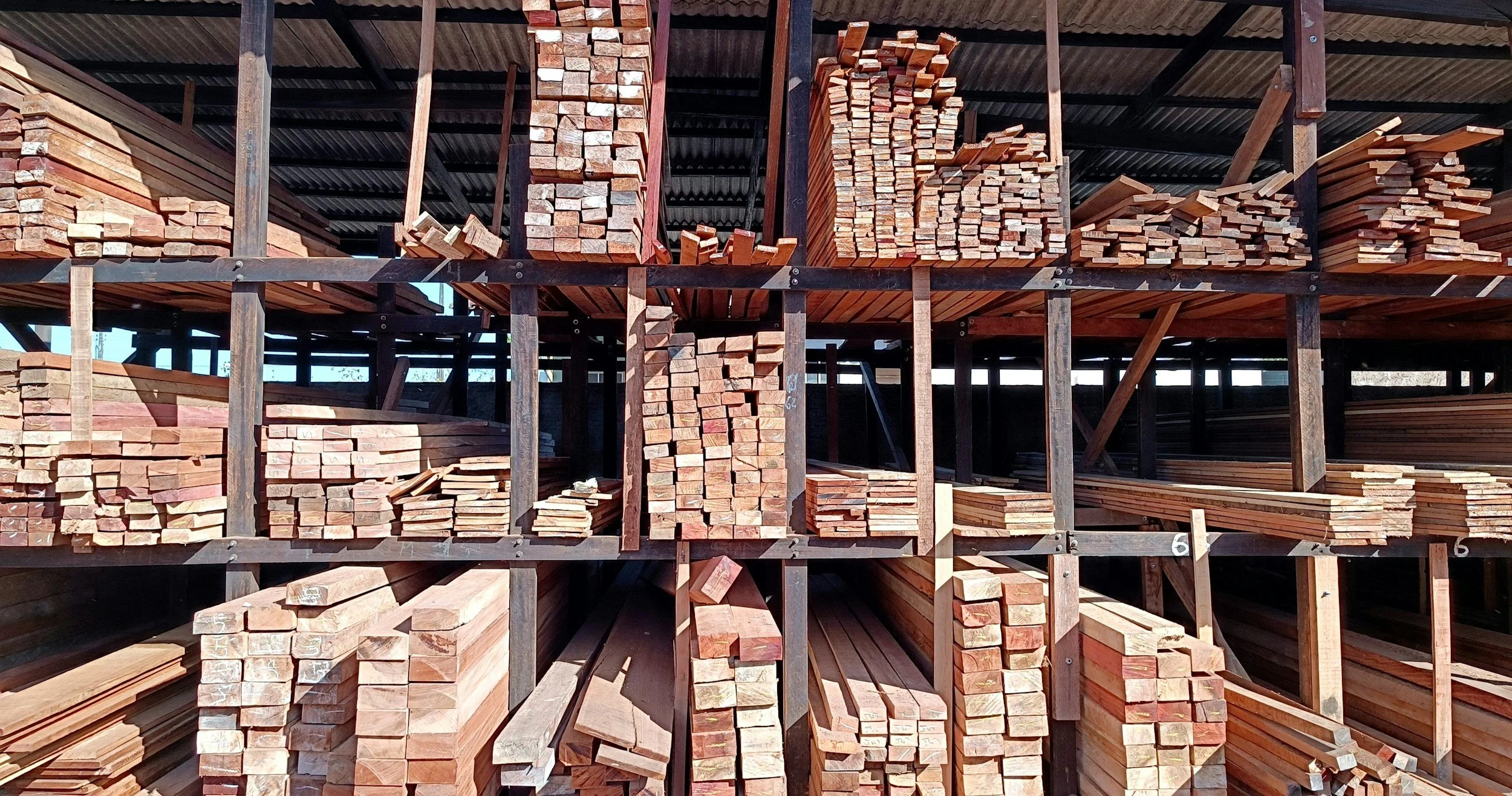 Pile of various cut wooden planks and beams stored on a multi-level wooden scaffold in a lumber yard.