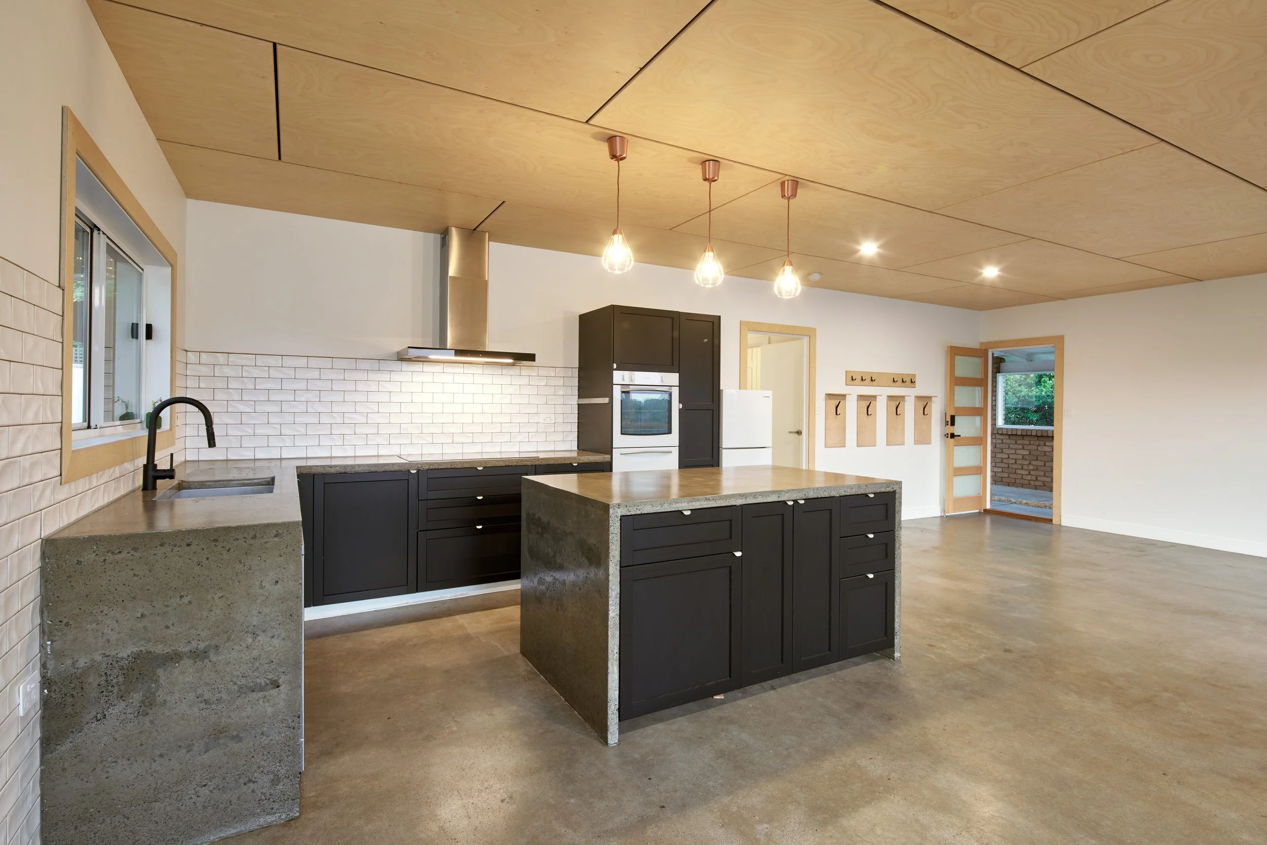 Modern kitchen with black cabinets, a concrete island, a white subway tile backsplash, and pendant lights with exposed bulbs.