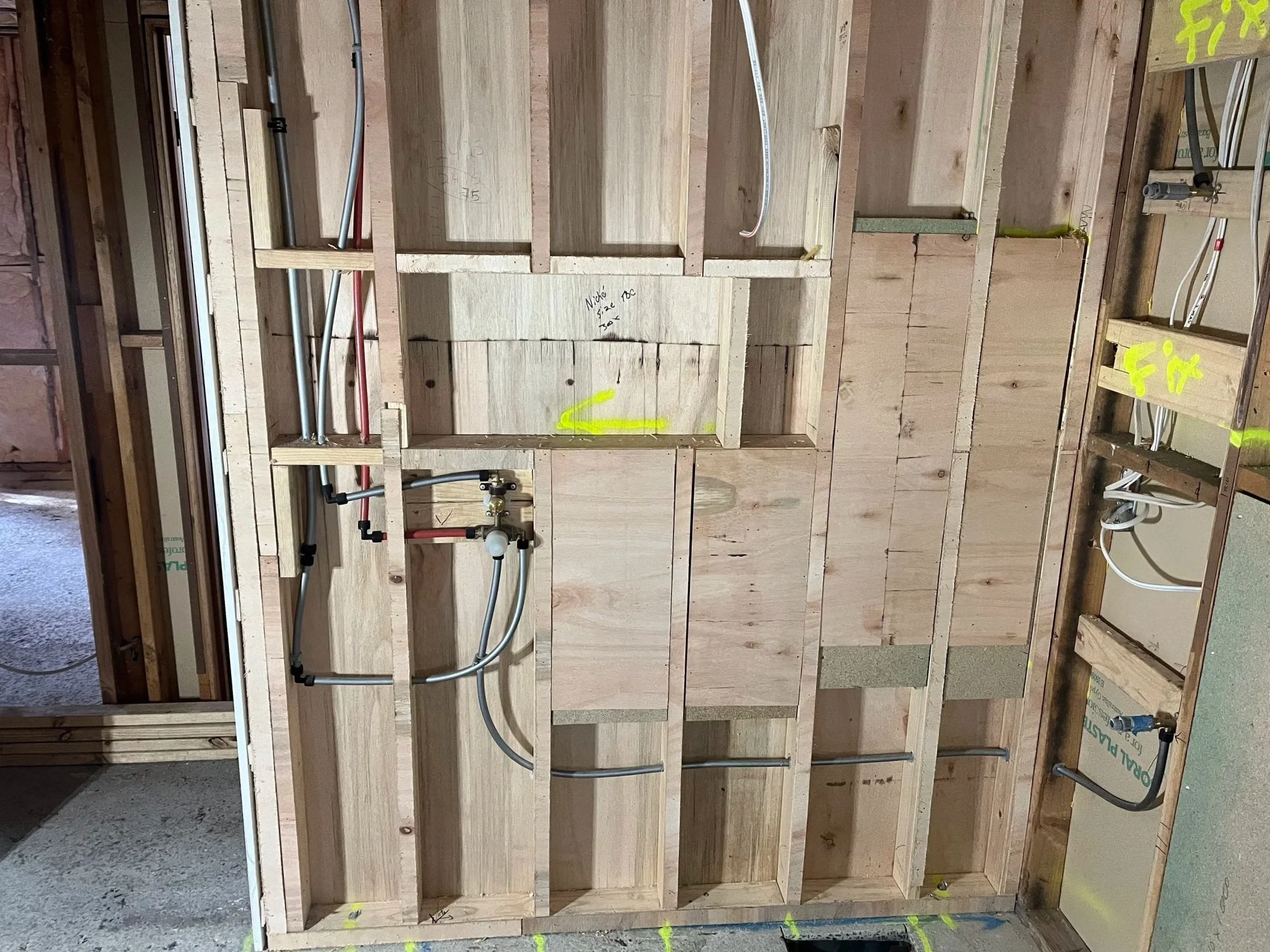 Construction site showing wooden framing for walls with electrical and plumbing rough-ins installed.