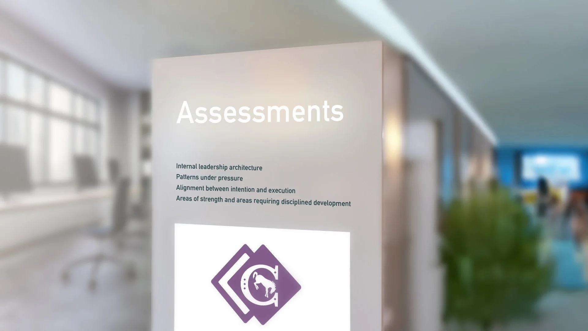 A sign titled 'Assessments' listing topics like leadership, pressure, alignment, areas of strength, and discipline, with a purple logo on a white background in a modern office setting.