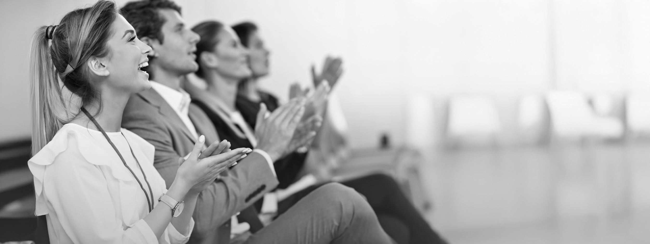 Group of people sitting in an auditorium, clapping and smiling, watching a presentation or performance.