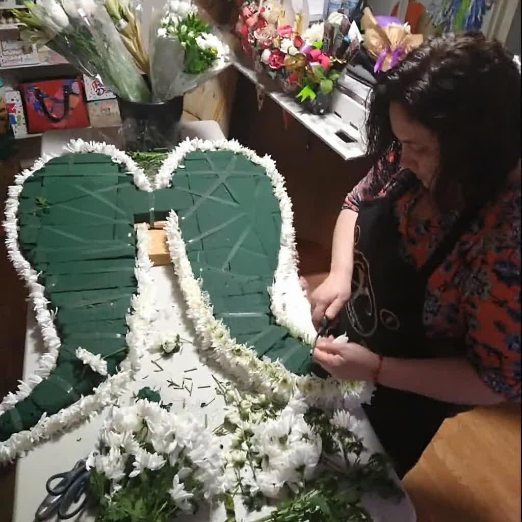 Mujer decorando un gran ramo de flores con letras en forma de 'R' y 'A' en un taller de arreglos florales.