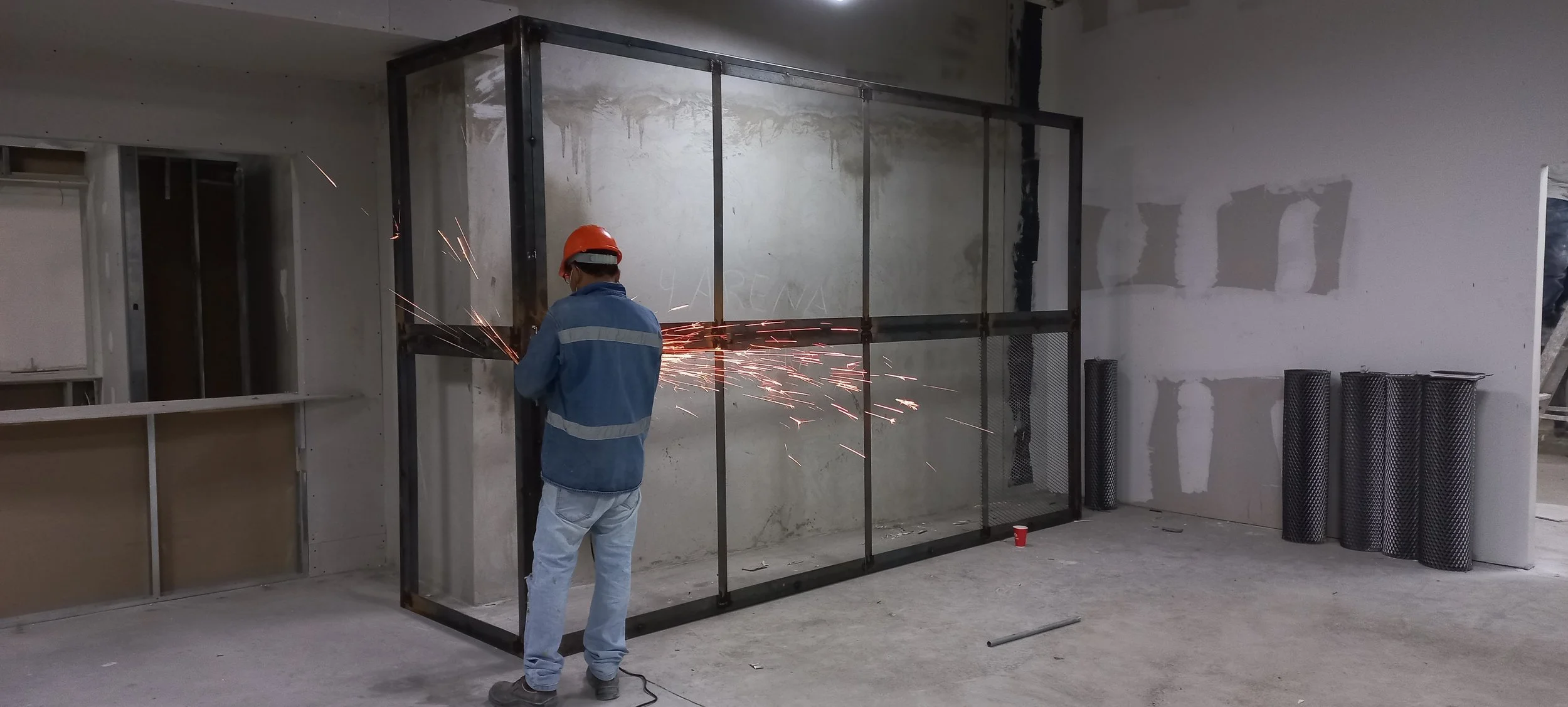 Una persona con casco de seguridad y ropa de trabajo usando una herramienta de soldadura en un espacio interior en construcción.