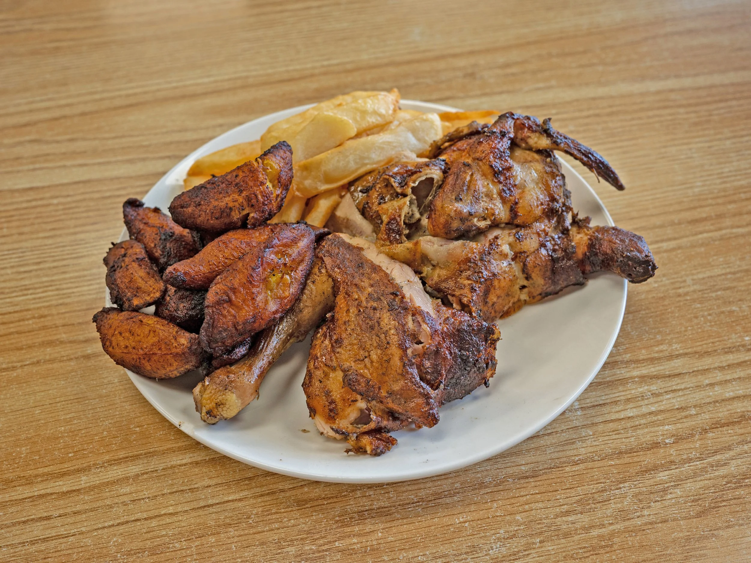 Plate of fried chicken, potato wedges, potato chips, and fried plantains on a wooden table.