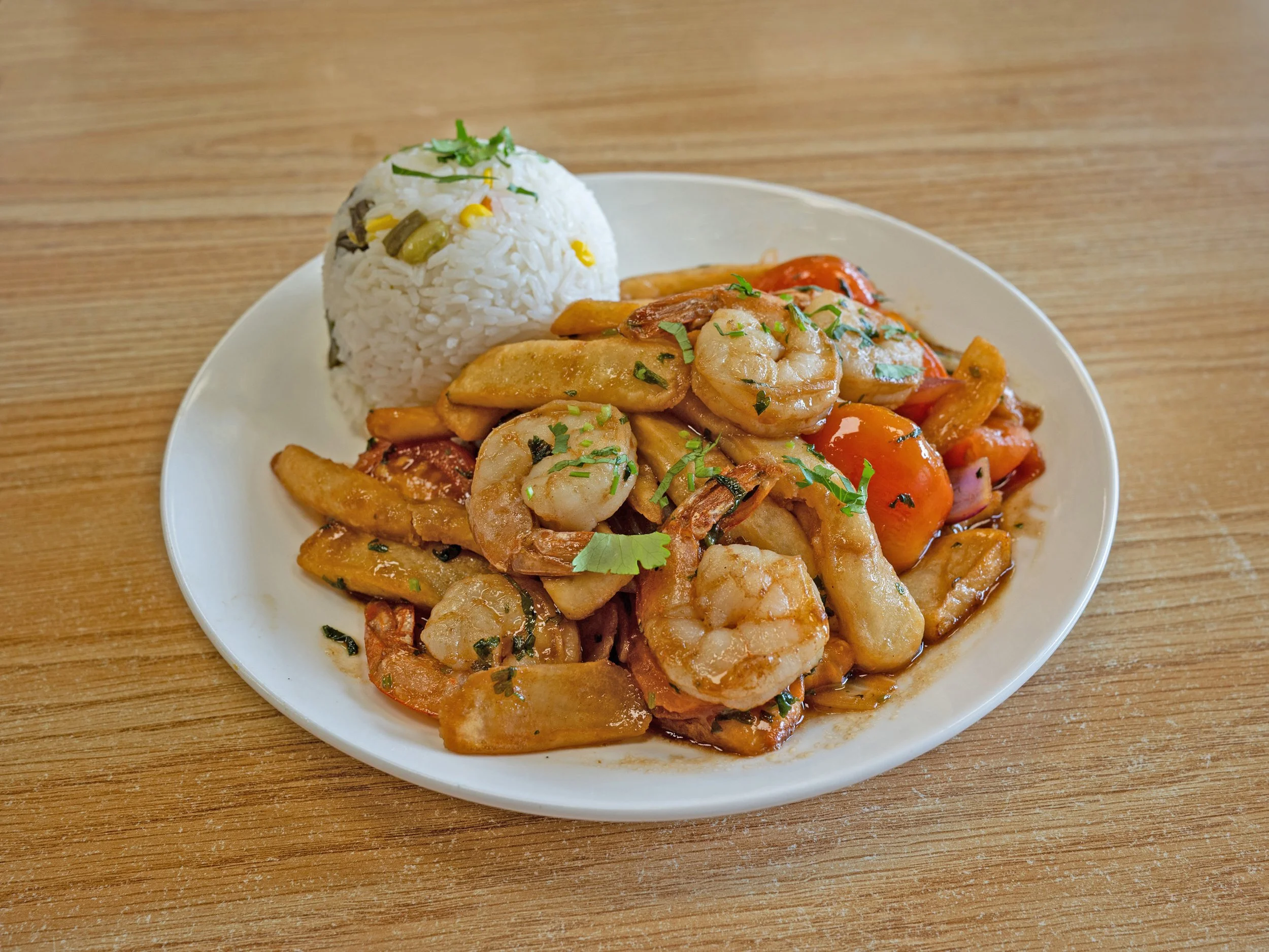 Shrimp and chicken stir-fry with vegetables served with a side of rice garnished with chopped herbs on a white plate