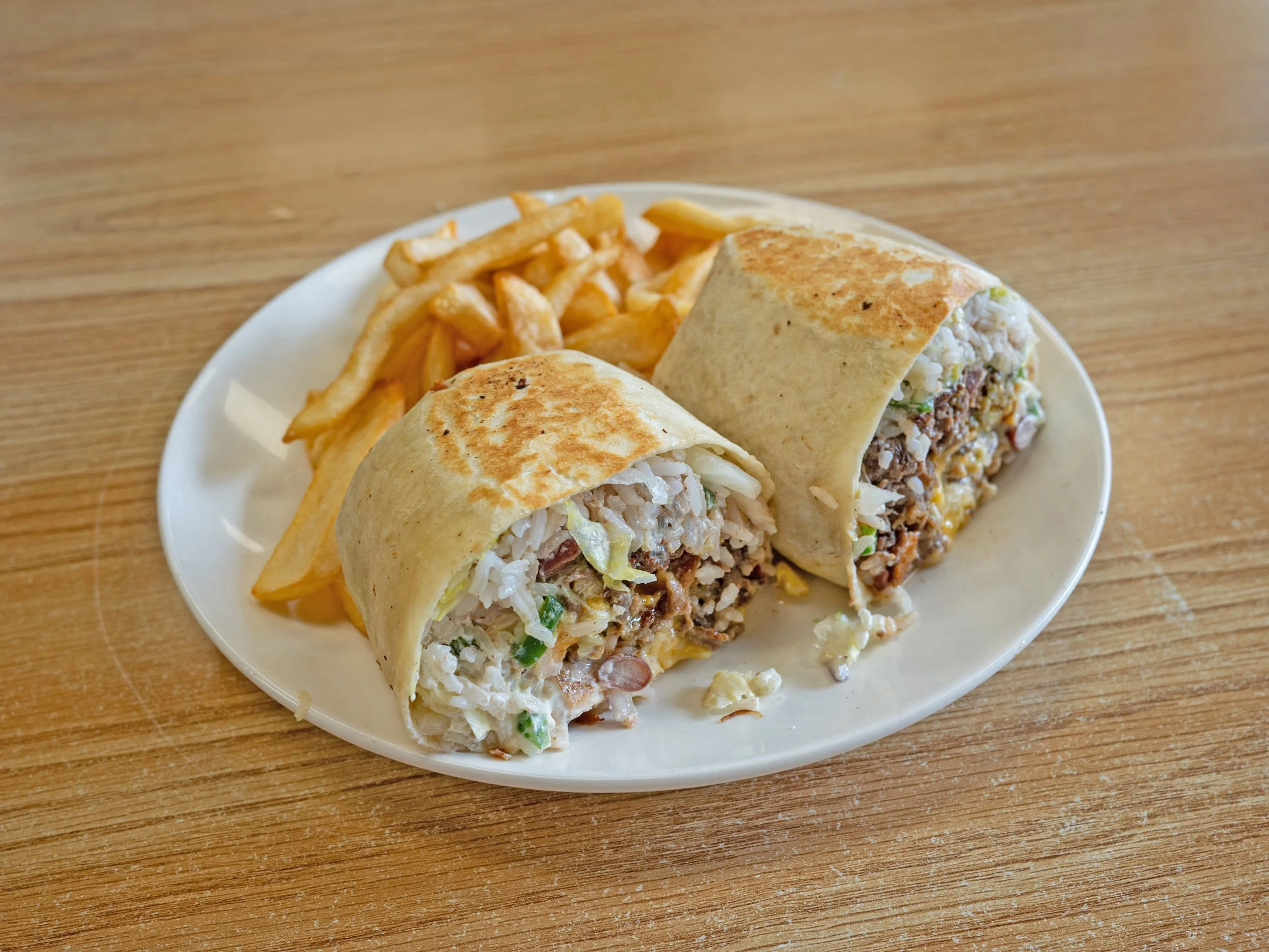 A plate of chicken and rice burrito wraps with French fries on a wooden table.