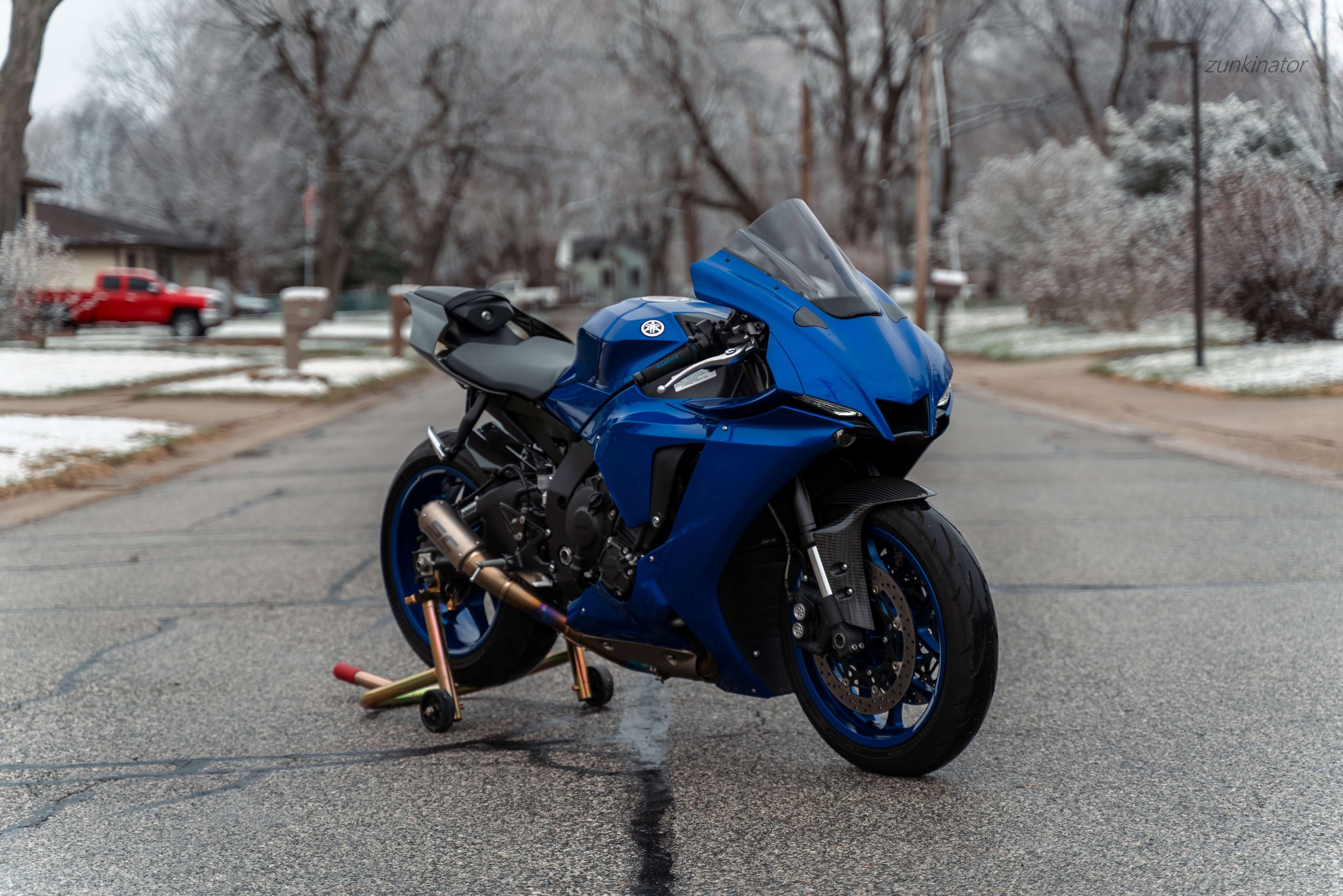 A blue Yamaha sport motorcycle parked on a street in a suburban neighborhood with snow on the ground.