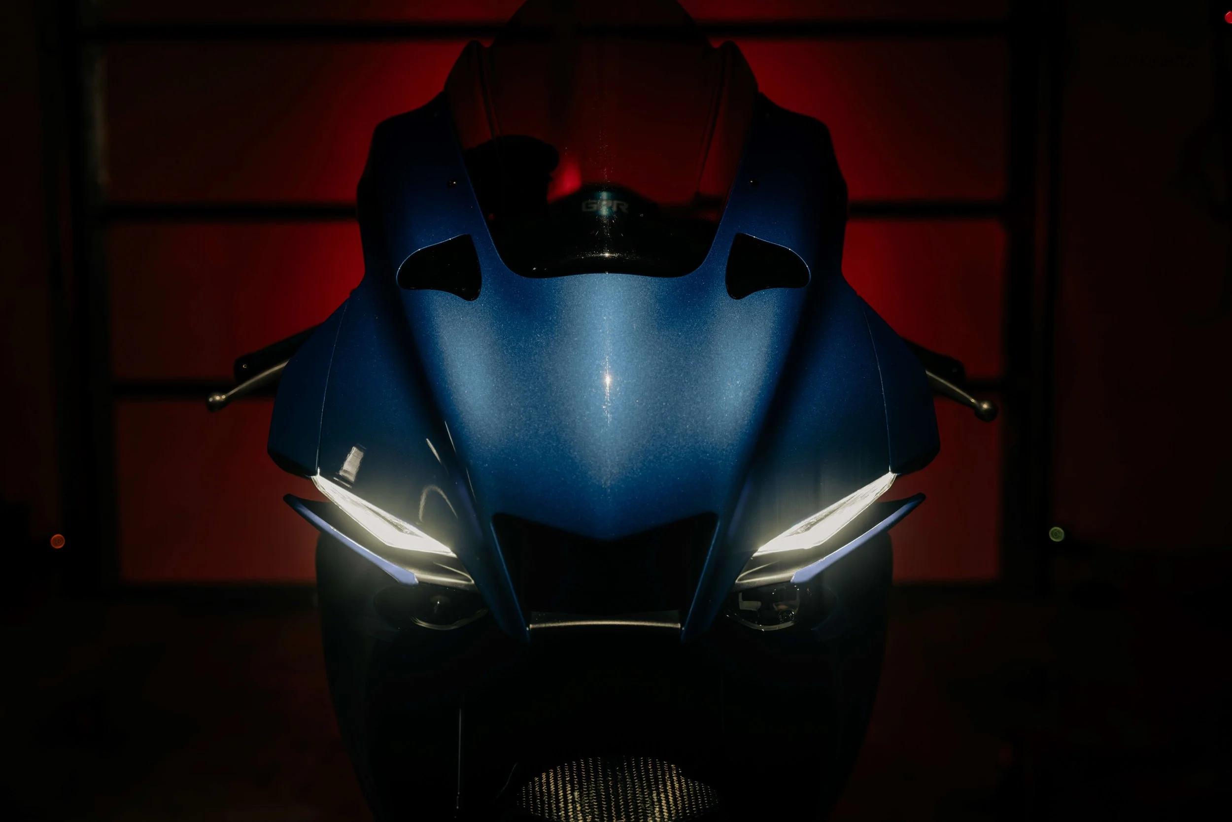 Front view of a blue sport motorcycle with bright headlights on in a dimly lit garage.
