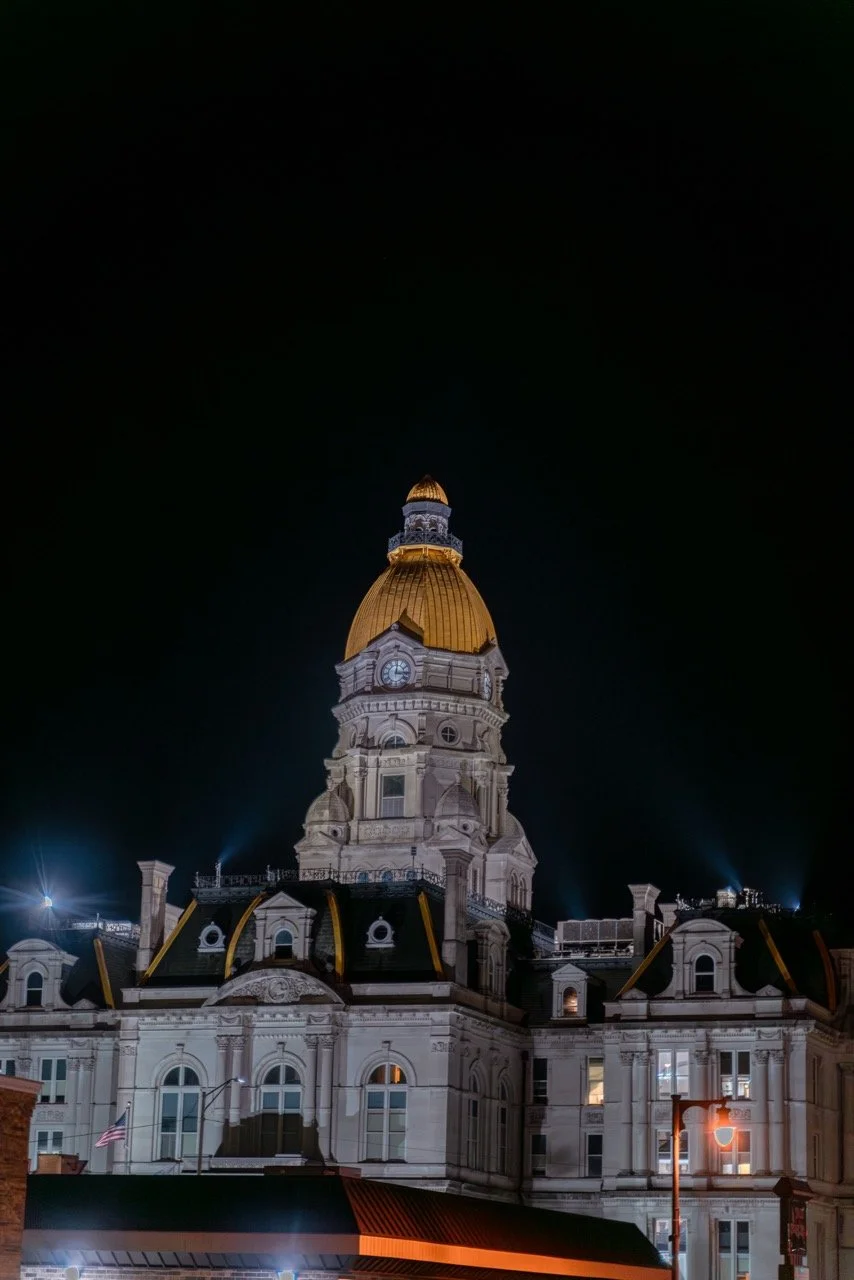 Night view of a historic building with a large, gold-colored domed roof, illuminated against a dark sky