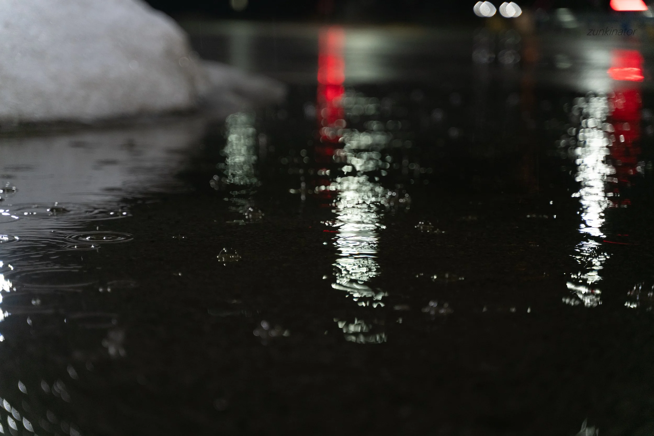 Close-up of a wet street surface reflecting streetlights and vehicle lights at night.