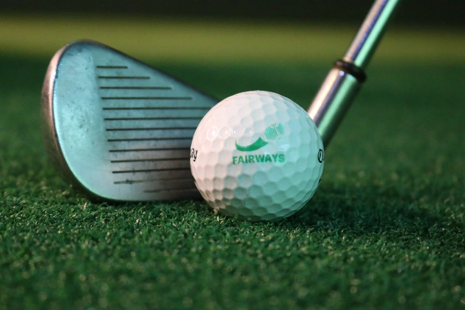 A golf ball with the brand 'Fairways' in front of a golf club on a green grass surface.