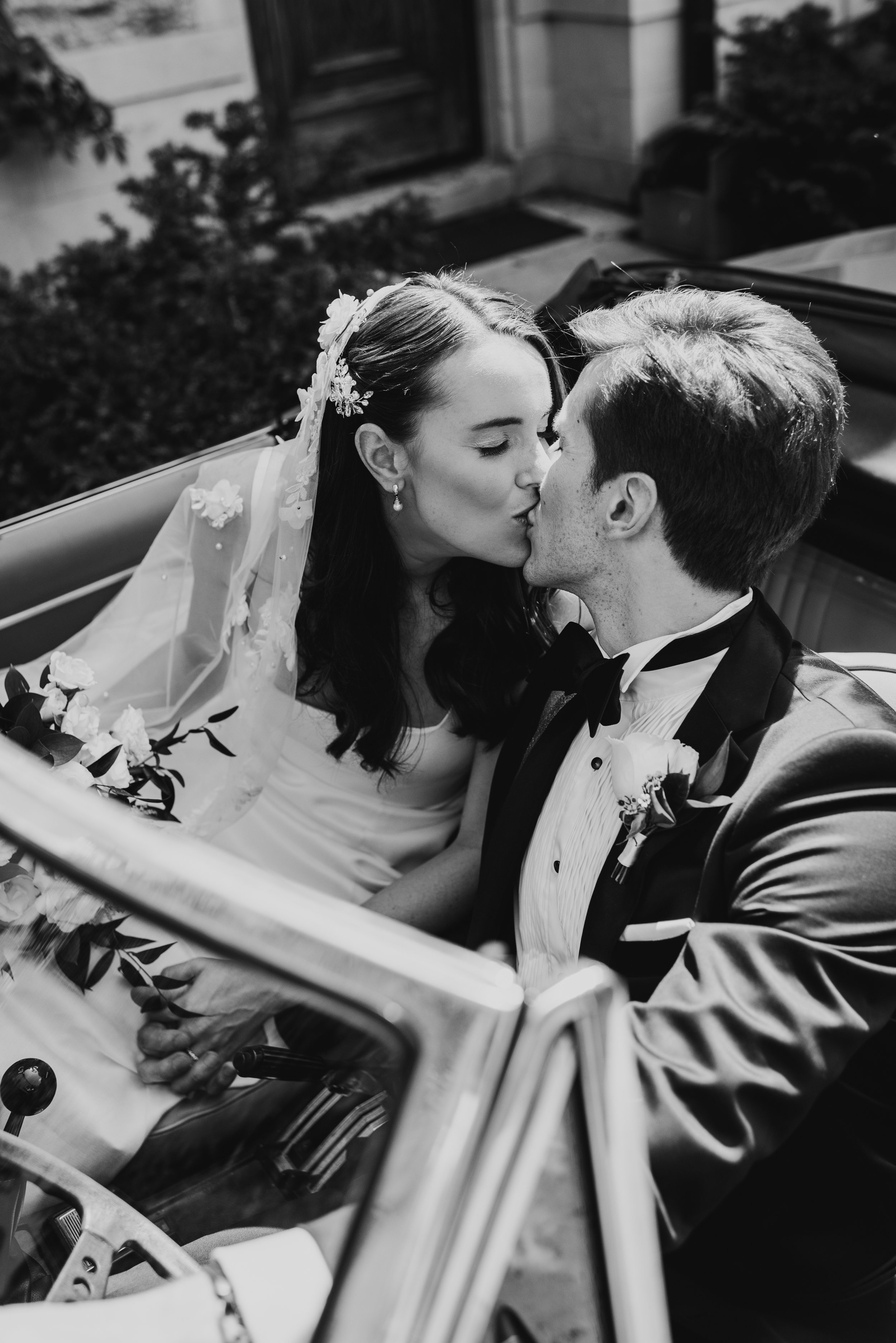 black and white image of a bride and groom kissing in a convertable. The bride is wearing an heirloom veil. This photo was taken at St. Paul College Club.