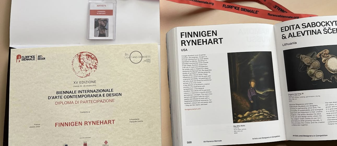 Open art book featuring information about artist Finnigen Ryenhart, with a photograph titled 'Boy Who Waits' on the right page. A conference badge and a diploma of participation for Finnigen Ryenhart are also visible.