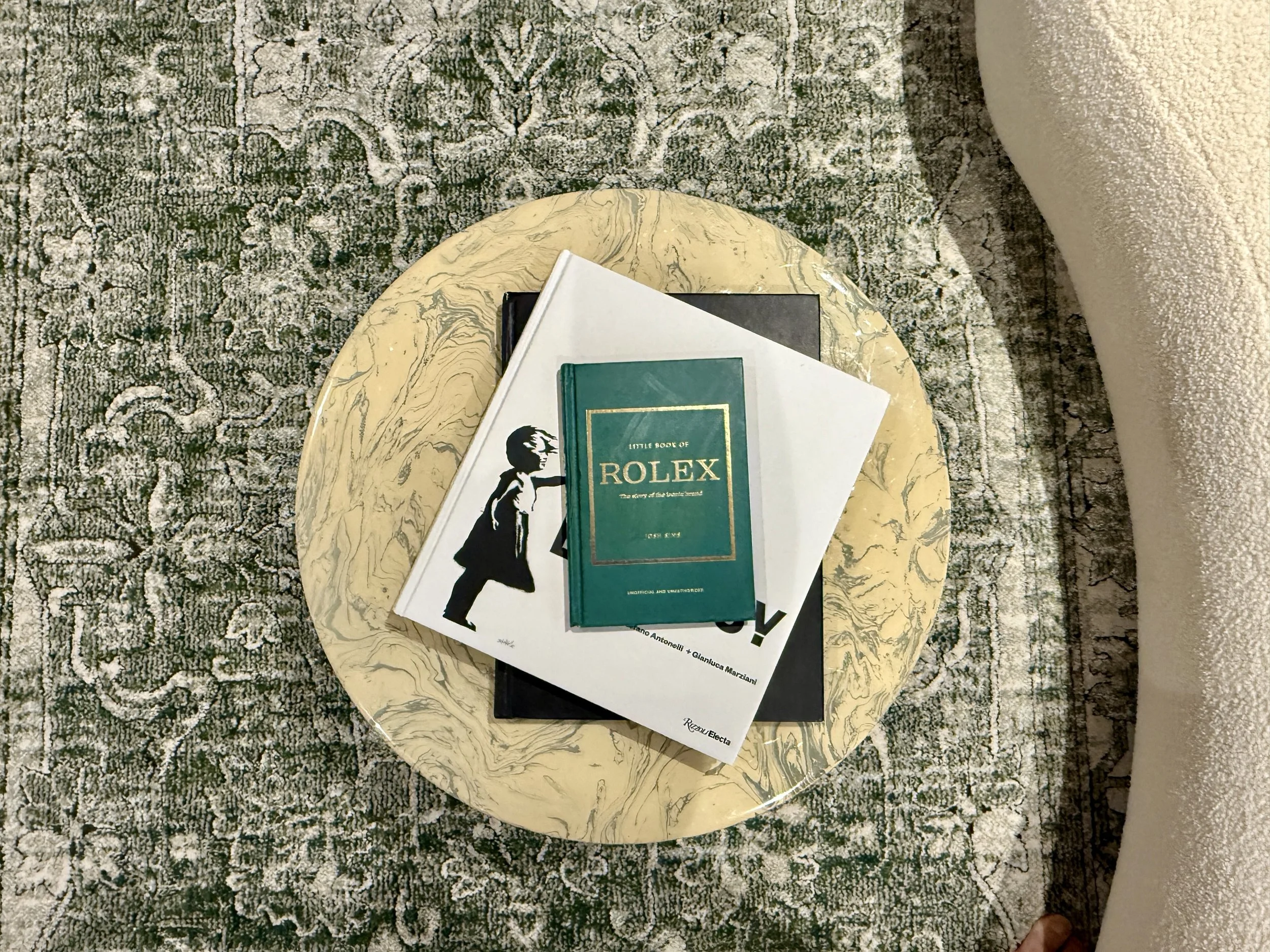 A round marble table with books and magazines on top, placed on a patterned rug in a living room.
