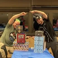 Two people are playing Jenga at a table, each holding a piece of the tower. There are multiple stacks of Jenga blocks, some with a red garnet colored box and others with a light blue box as prizes or decorations, on the table.