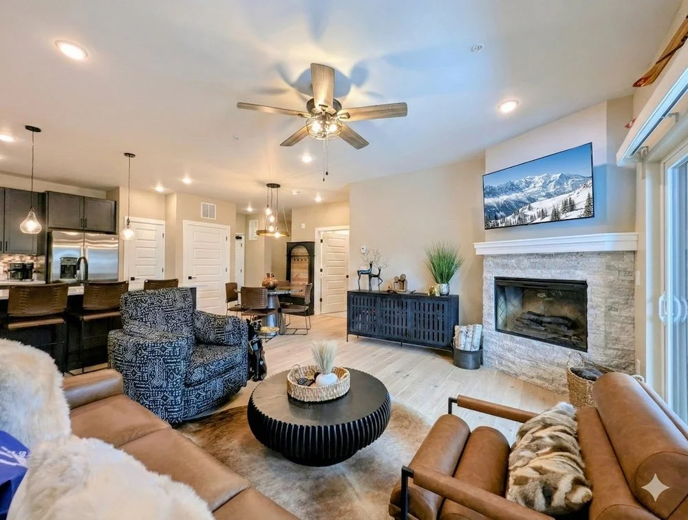 Modern accommodations in Keystone Colorado, a living room with leather and fabric seating, a fireplace with a TV above, a black sideboard, and a view of the kitchen with pendant lights and bar stools.