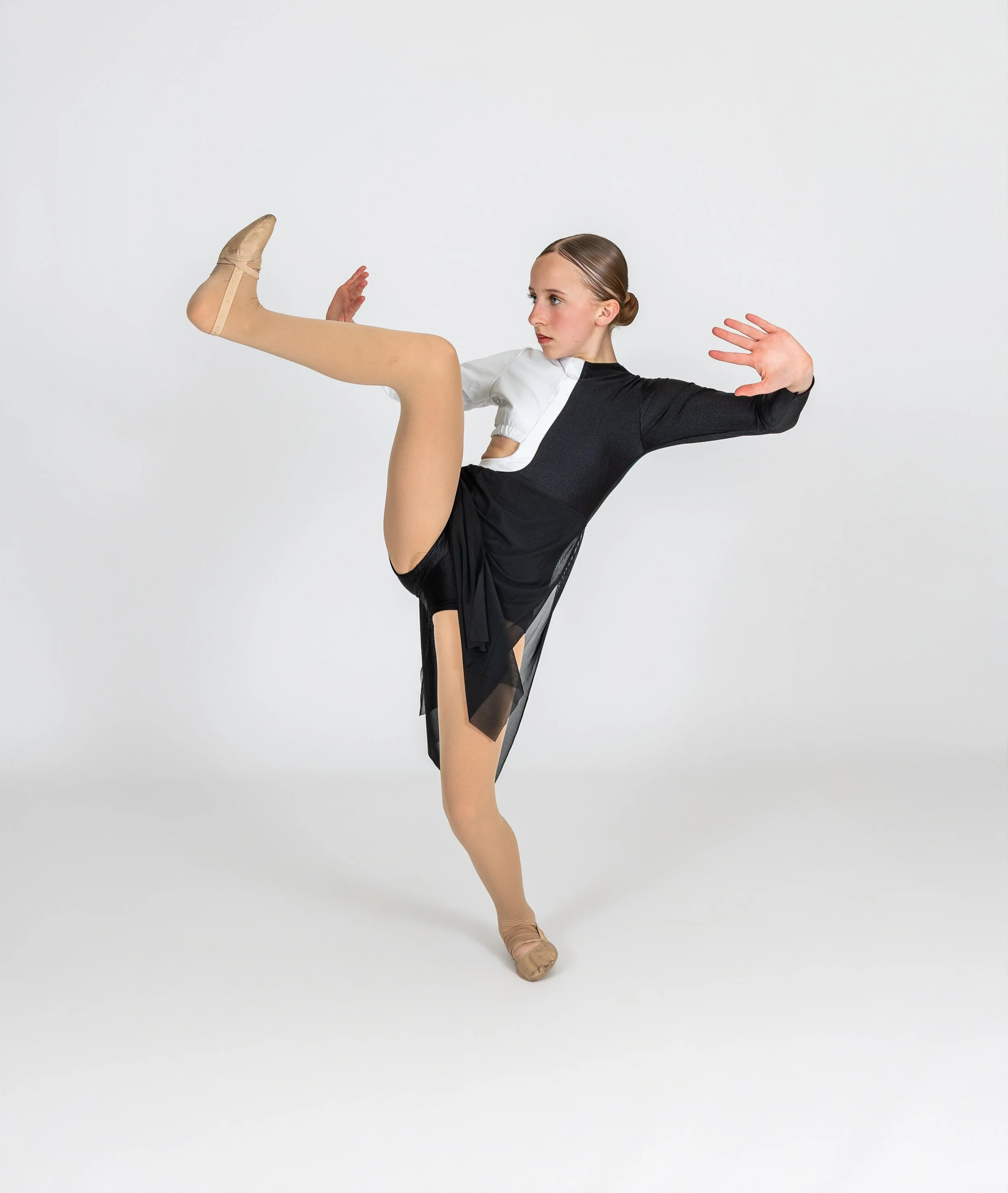 Dancer  in a black and white costume, balancing gracefully with one leg raised and arms outstretched, against a plain white background.