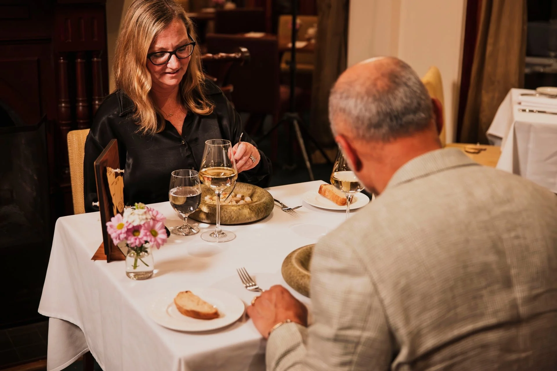 A couple dining at a restaurant, with the woman wearing glasses and the man with a bald head, enjoying a meal together.