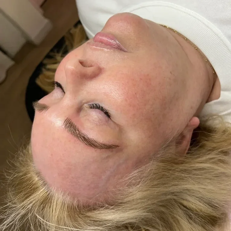 A woman with  micrbladed brows, blushed cheeks and closed eyes, lying down with her head tilted back