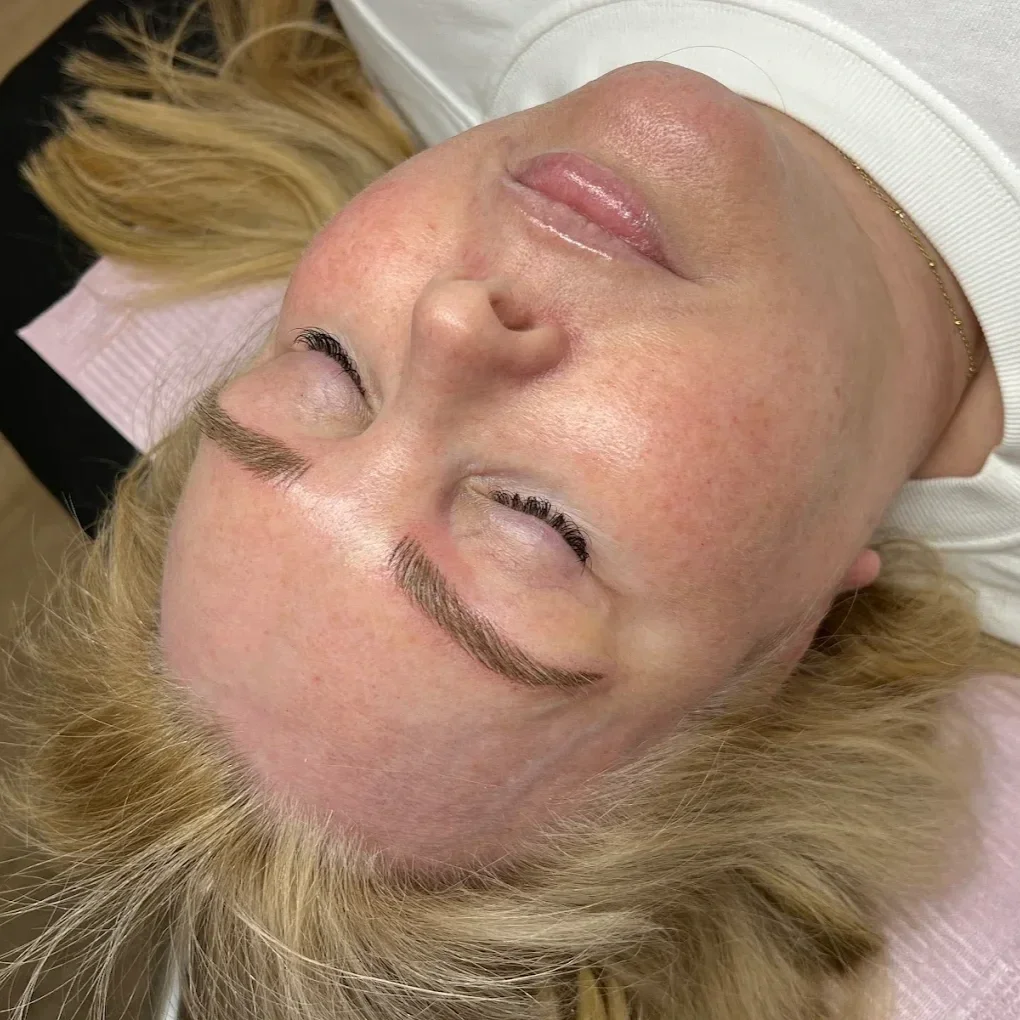 A woman lying down with microbladed brows, her eyes closed, showing her face with minimal makeup and well-groomed eyebrows.