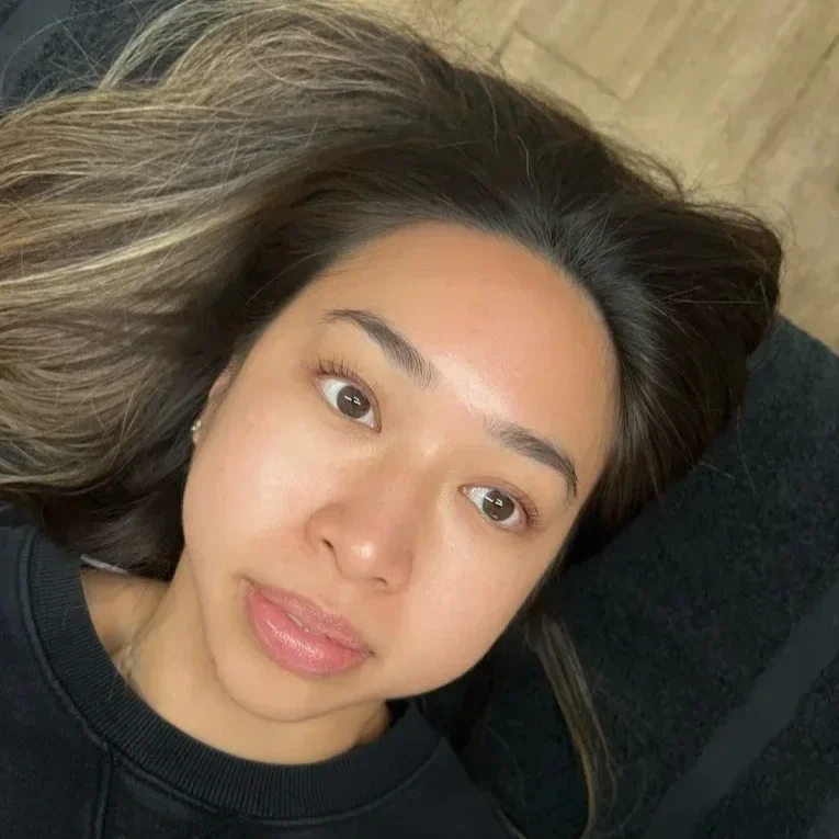 A woman with long brown hair lying on a black surface, looking up at the camera. lash lift