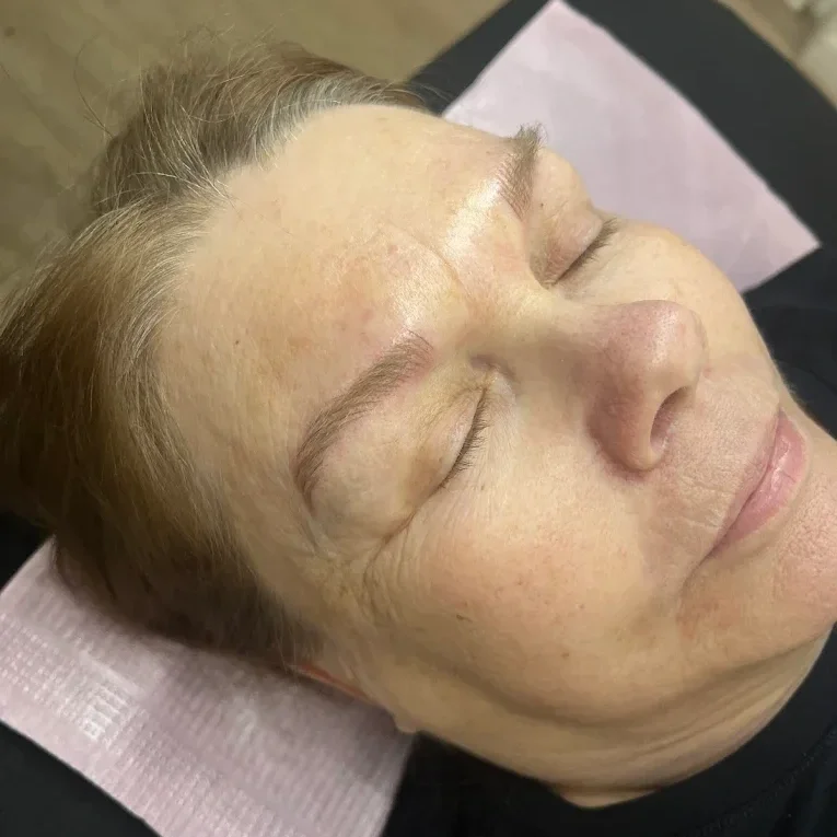 Close-up of a woman with closed eyes, relaxed, lying down with a skincare treatment on her face. microbladed brows