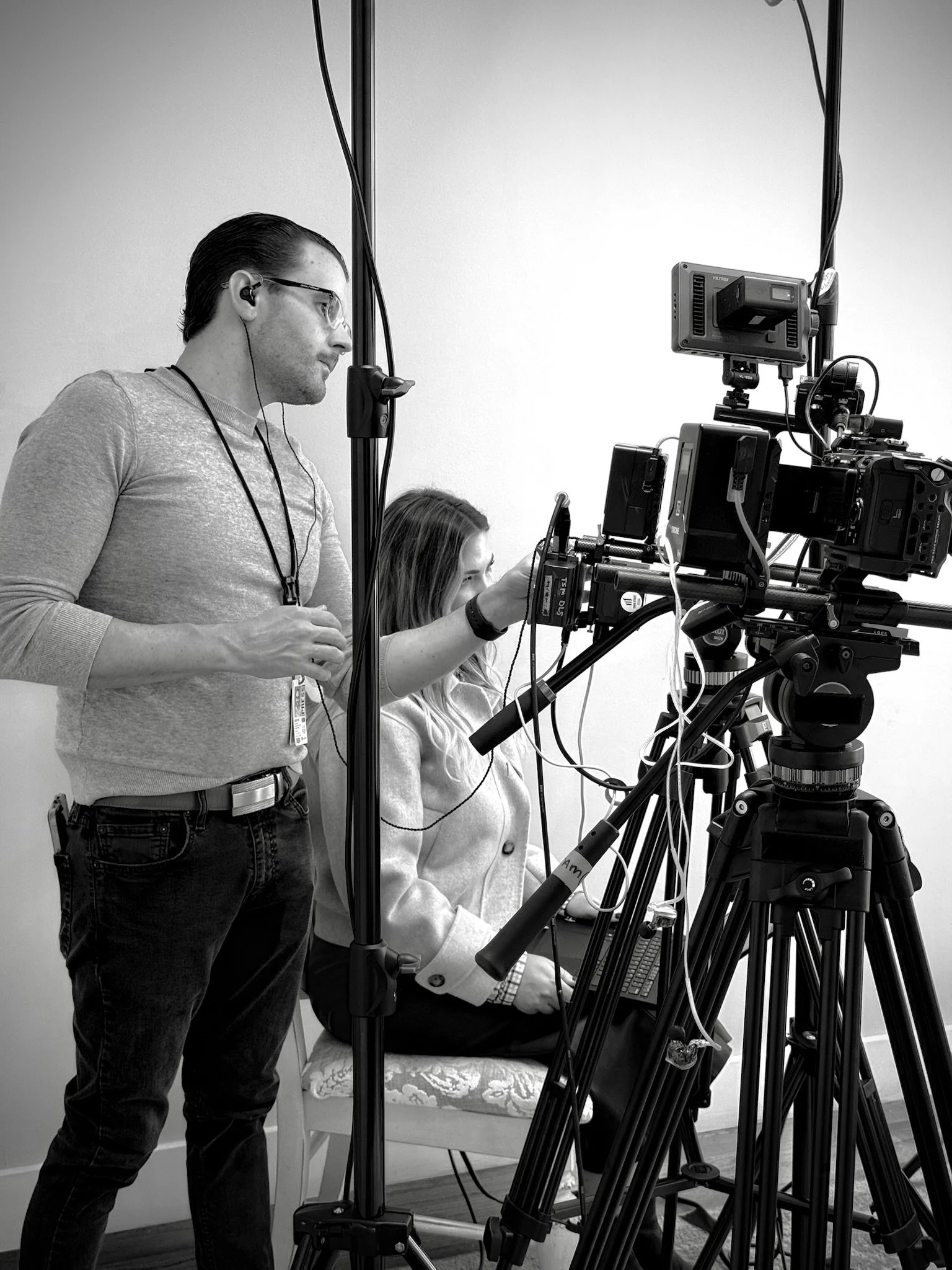 Two people operating a video camera setup in a studio, one standing and one sitting with a laptop.