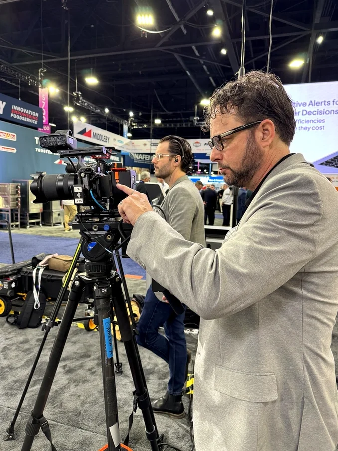 Professional camera operator filming video on the trade show floor during a large industry conference