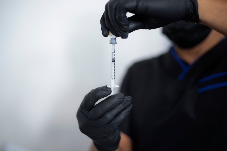 Person wearing black gloves and a black shirt filling a syringe with liquid.