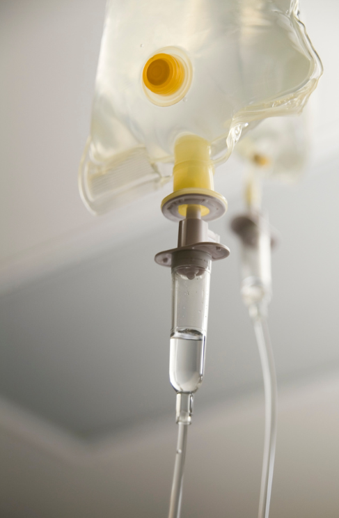 Close-up of an IV infusion set with a liquid bag hanging from a hospital ceiling.