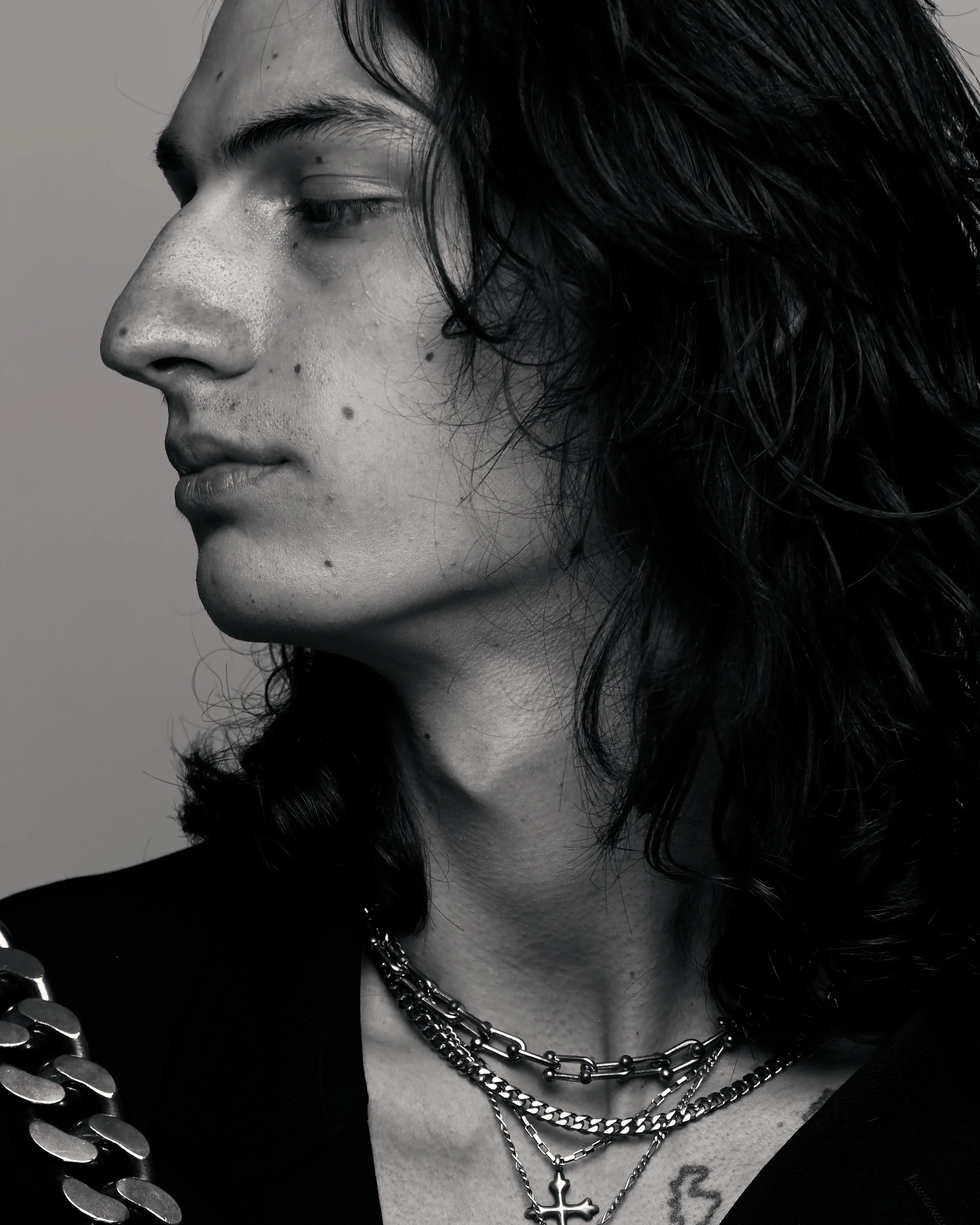 Black and white profile photo of a white model with long hair wearing silver necklaces