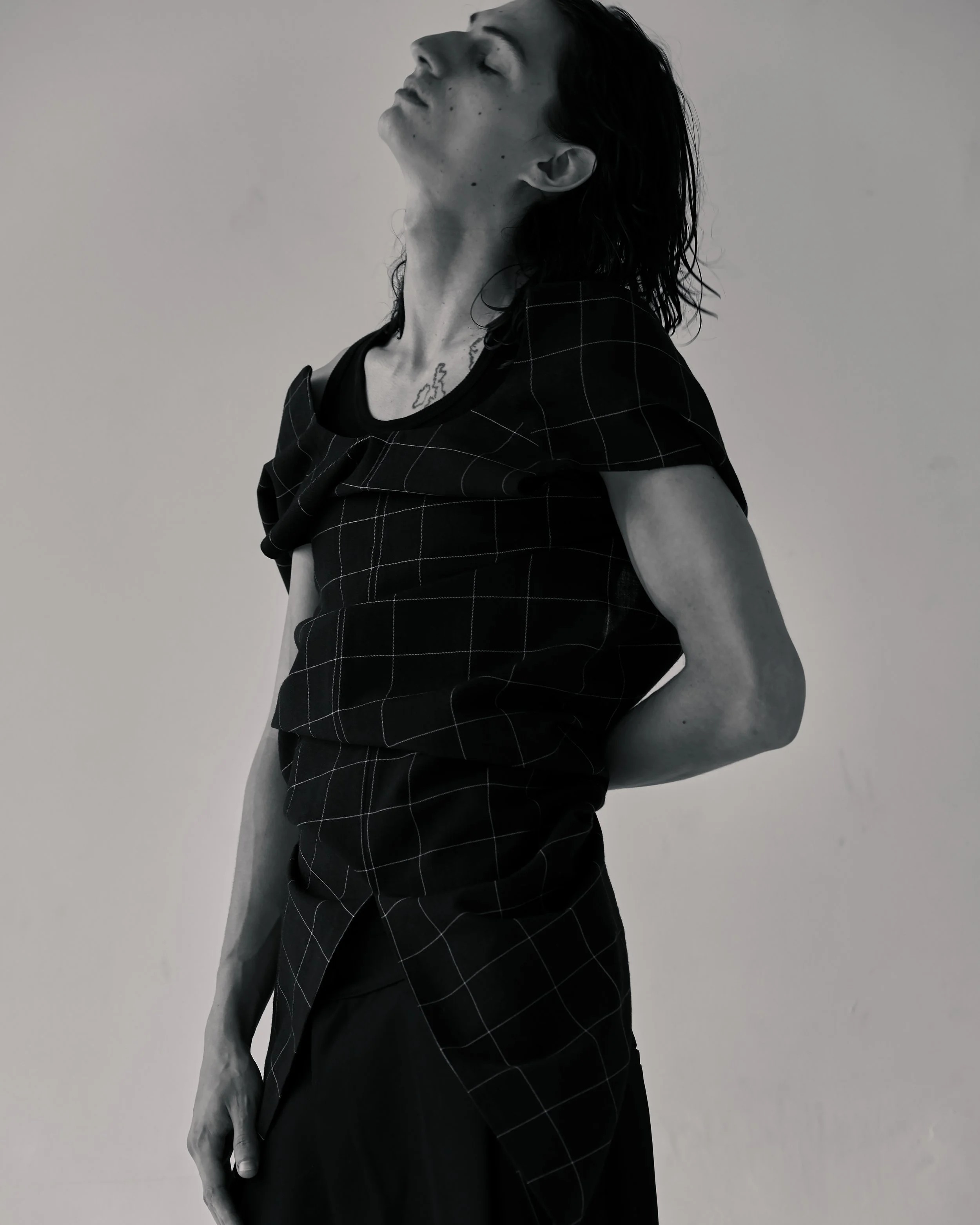 Black and white image of a white male model with long hair wearing a checked wool dress in a white studio