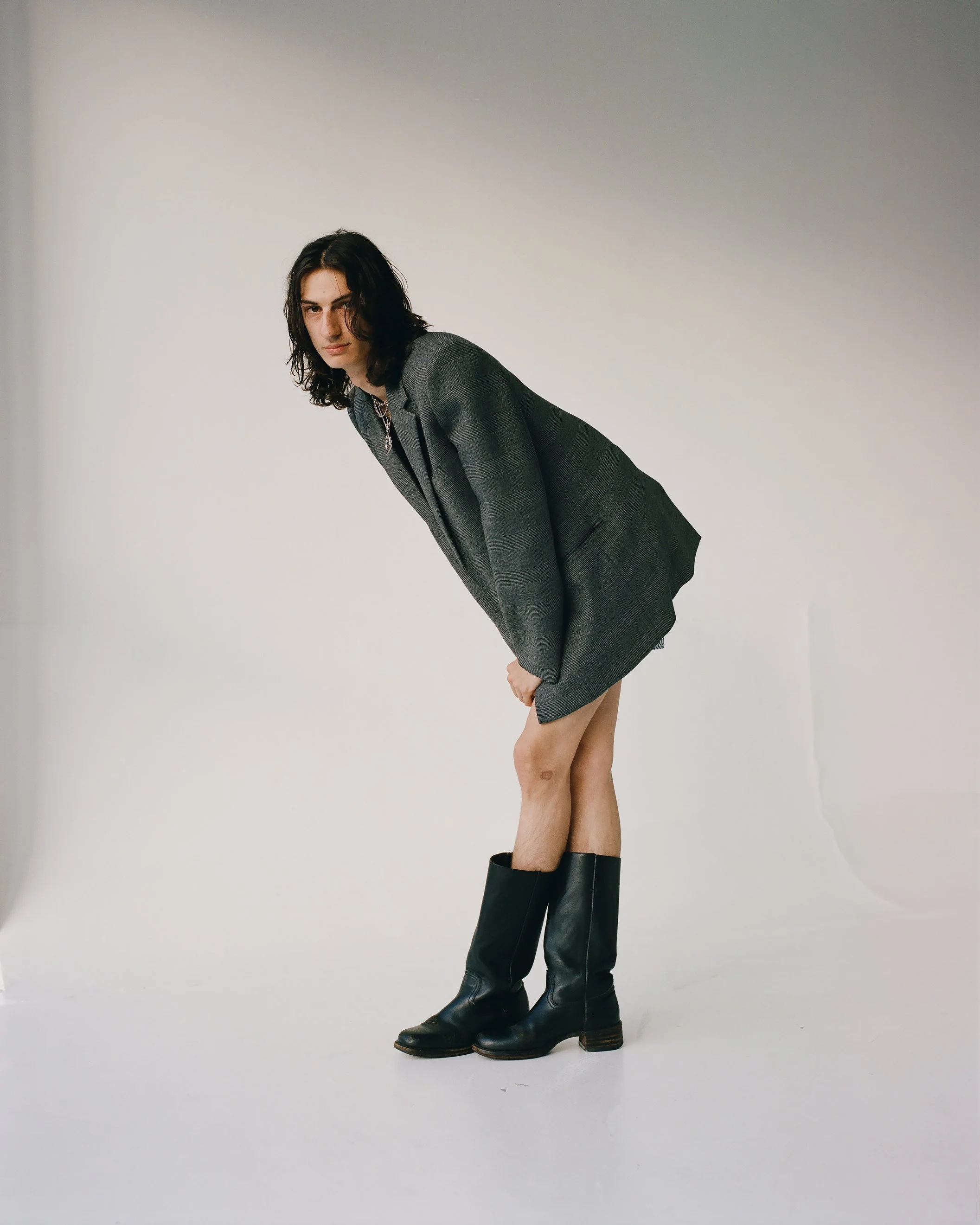 Image of a white male model with long brown hair wearing a grey blazer and black boots