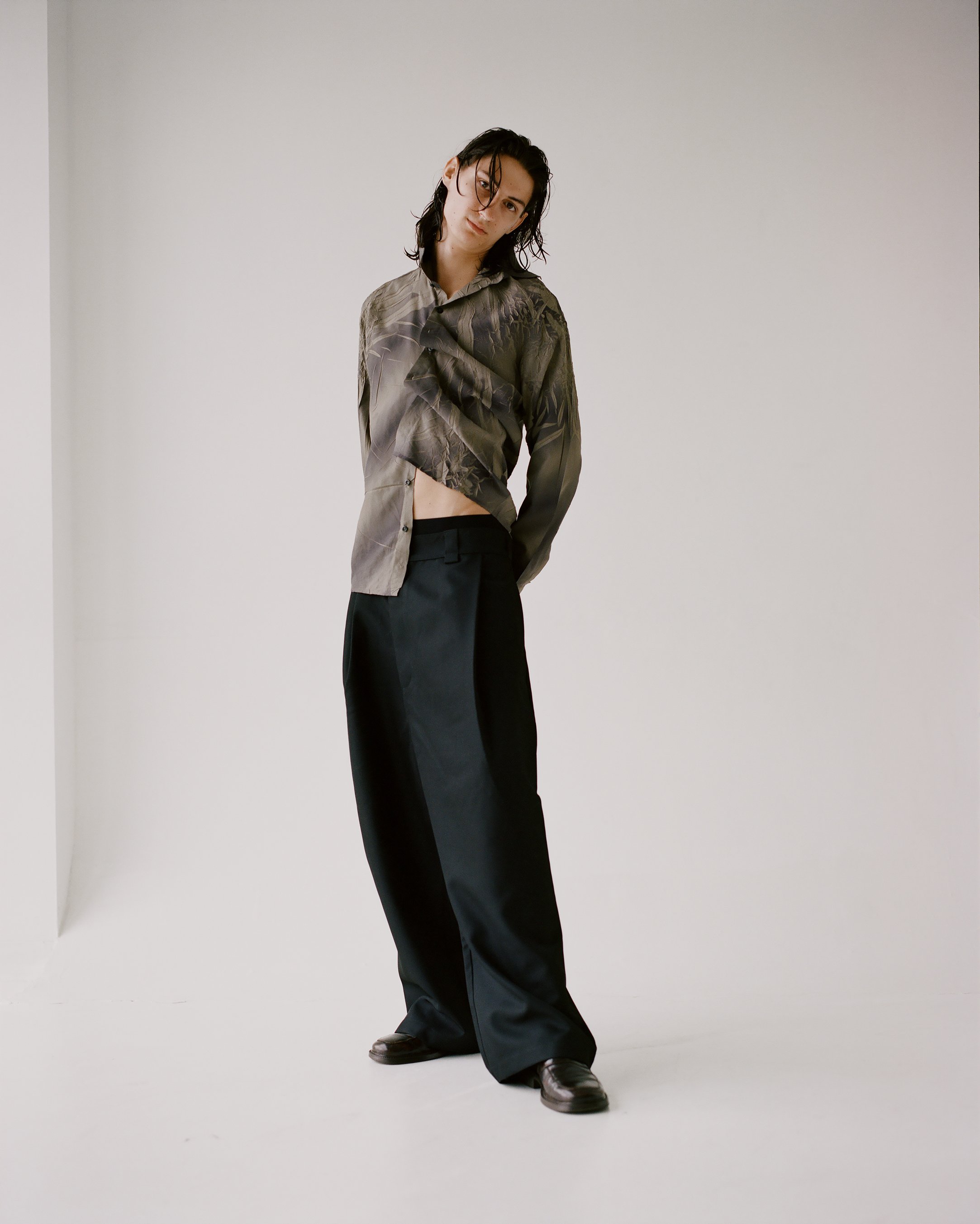 Image of a white male model with wet long hair wearing a scrunched up button down and black trousers in a white studio