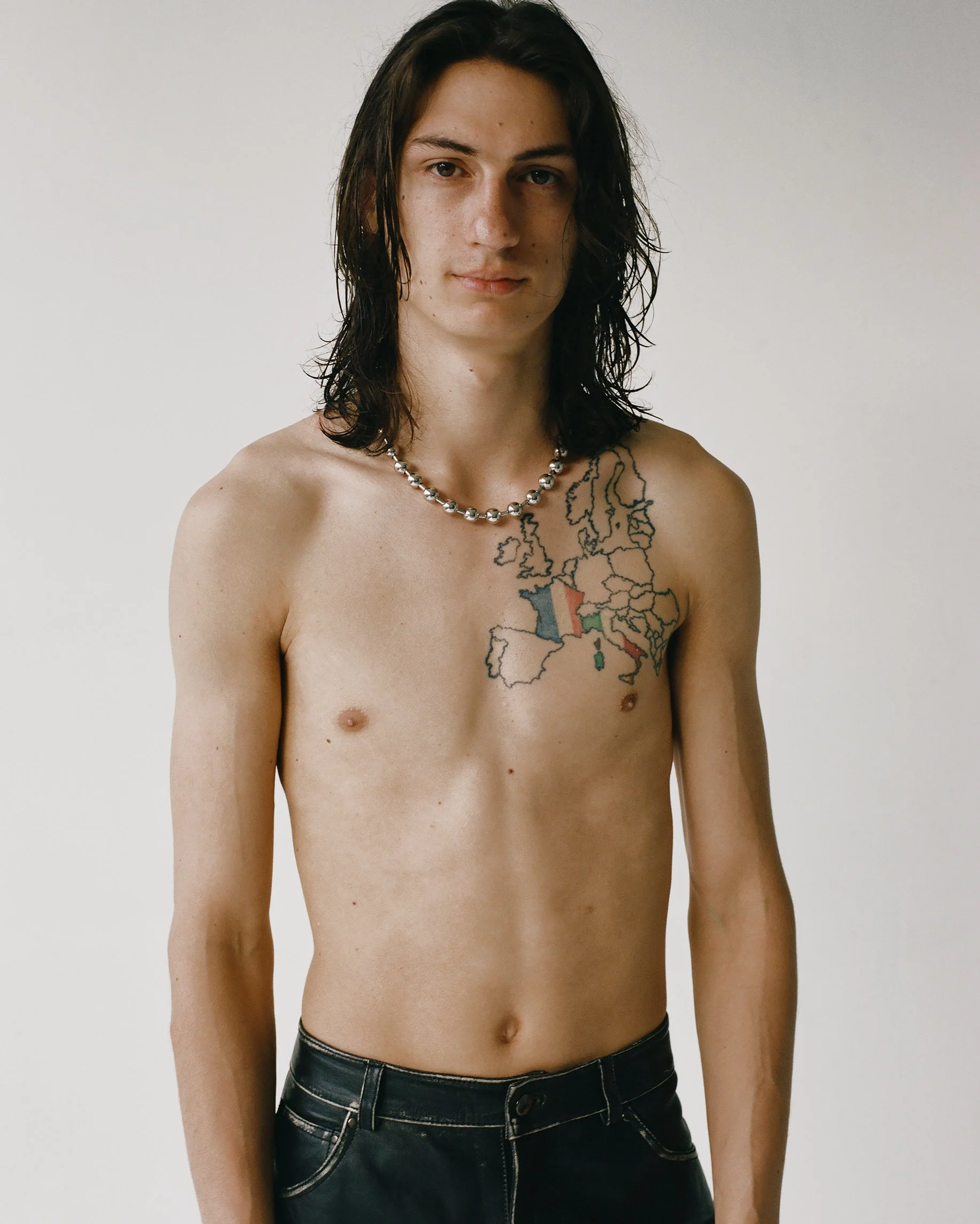 Image of a white male model with long wet brown hair wearing a silver chain and leather pants