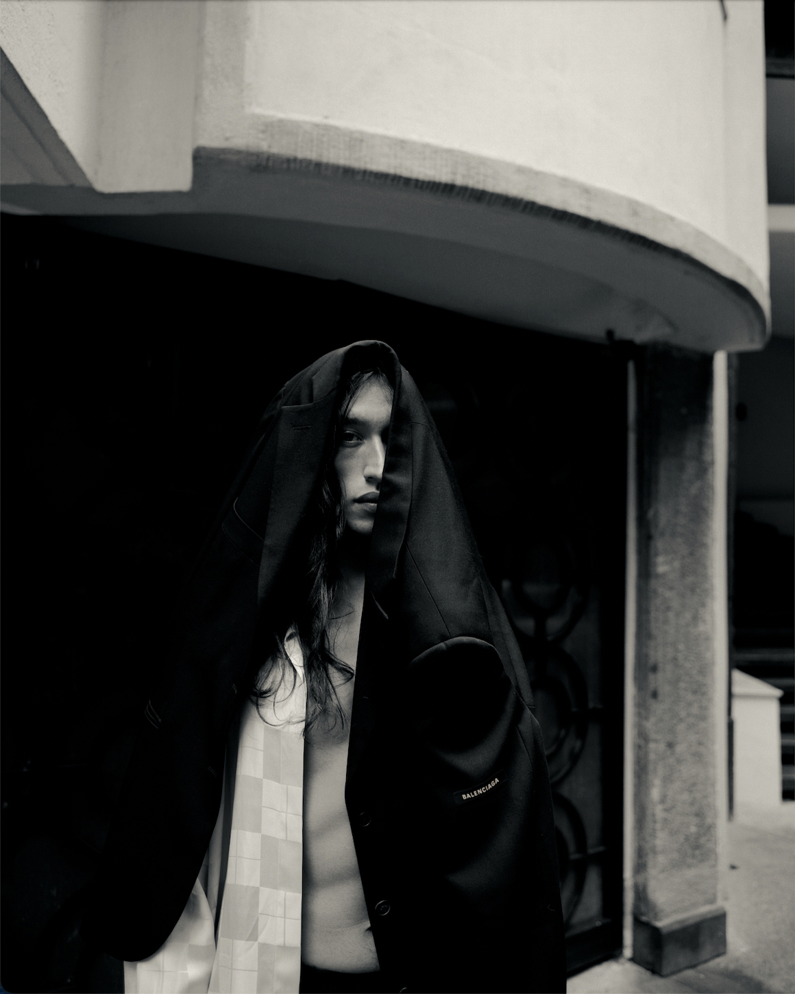 Black and white photo of a Mexican male model with a black blazer covering his head