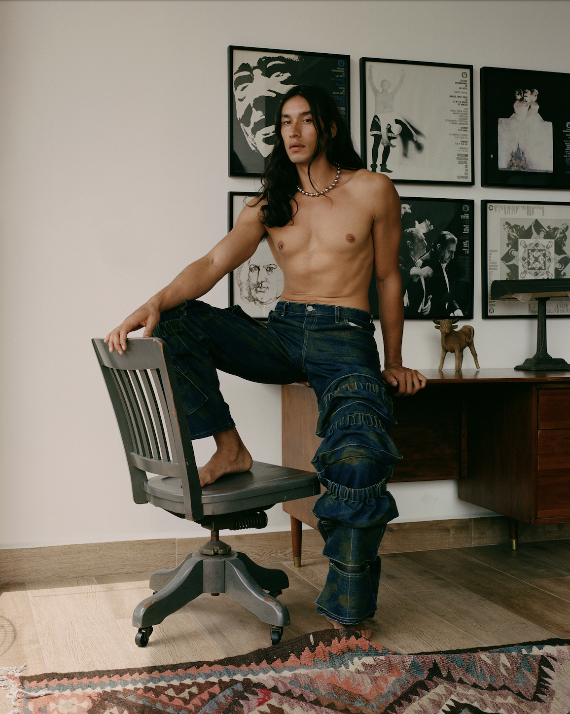 Photo of a Mexican male model sitting on a desk shirtless with green and blue cargo pants