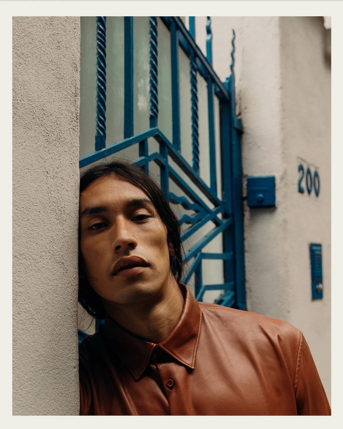 Close up image of a Mexican male model with long hair wearing a brown leather shirt
