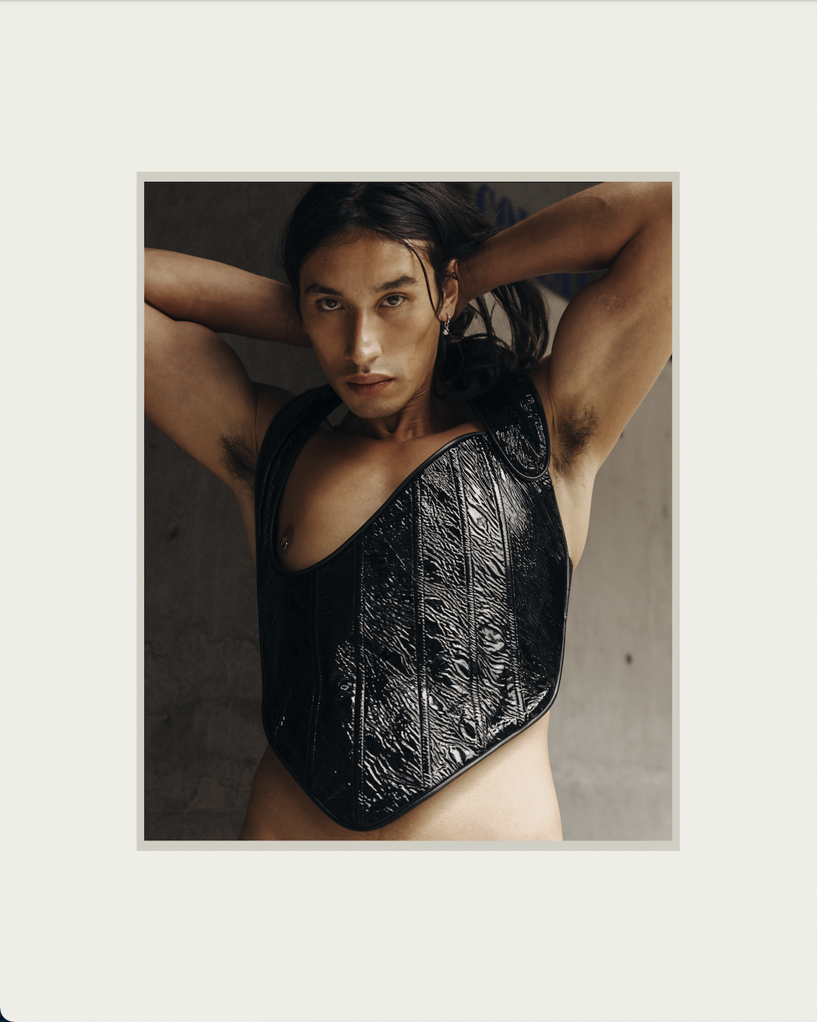 Portrait of a Mexican male model pulling his hair back with his hands while wearing a shiny black corset top