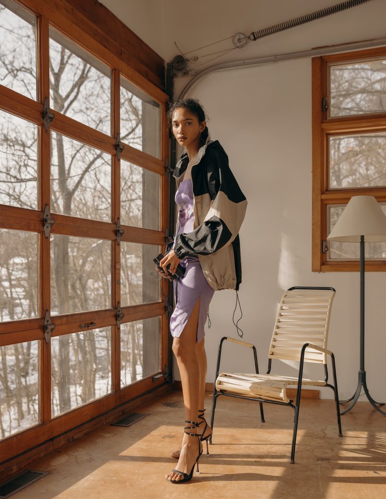 image of a latinx female model wearing a purple dress, heels, and a rain jacket inside a cabin