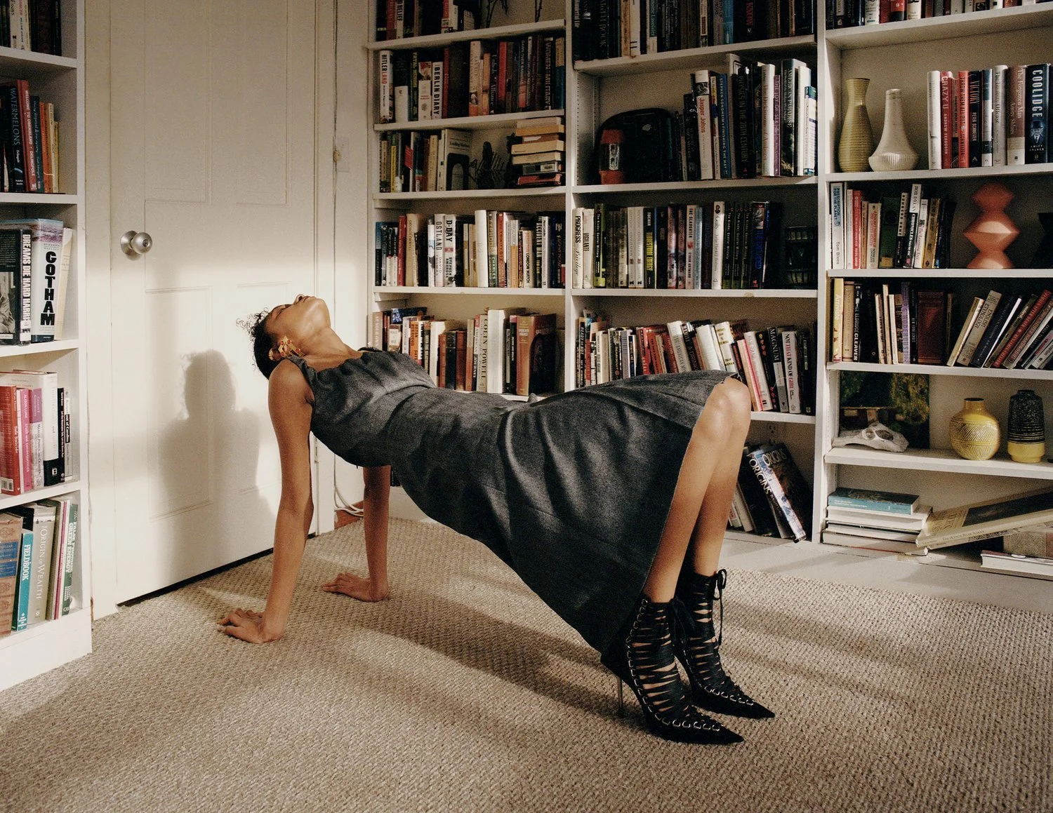 image of a latinx female model wearing a grey dress and black heels in a partial back bend in a library room