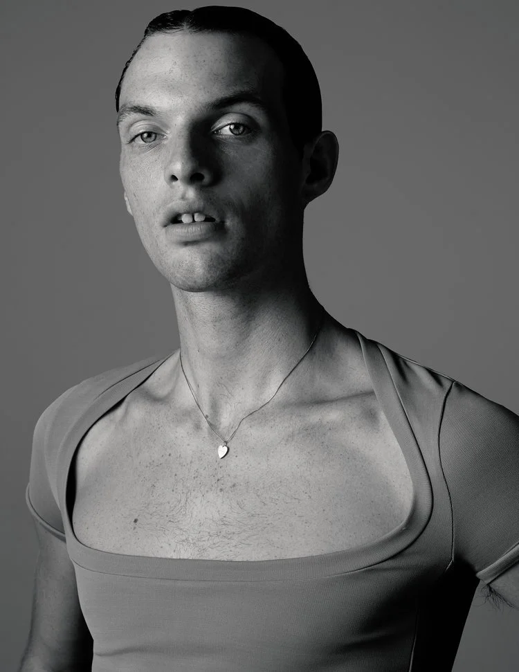 image of a white male model with slicked back hair wearing a wide neck top in a studio
