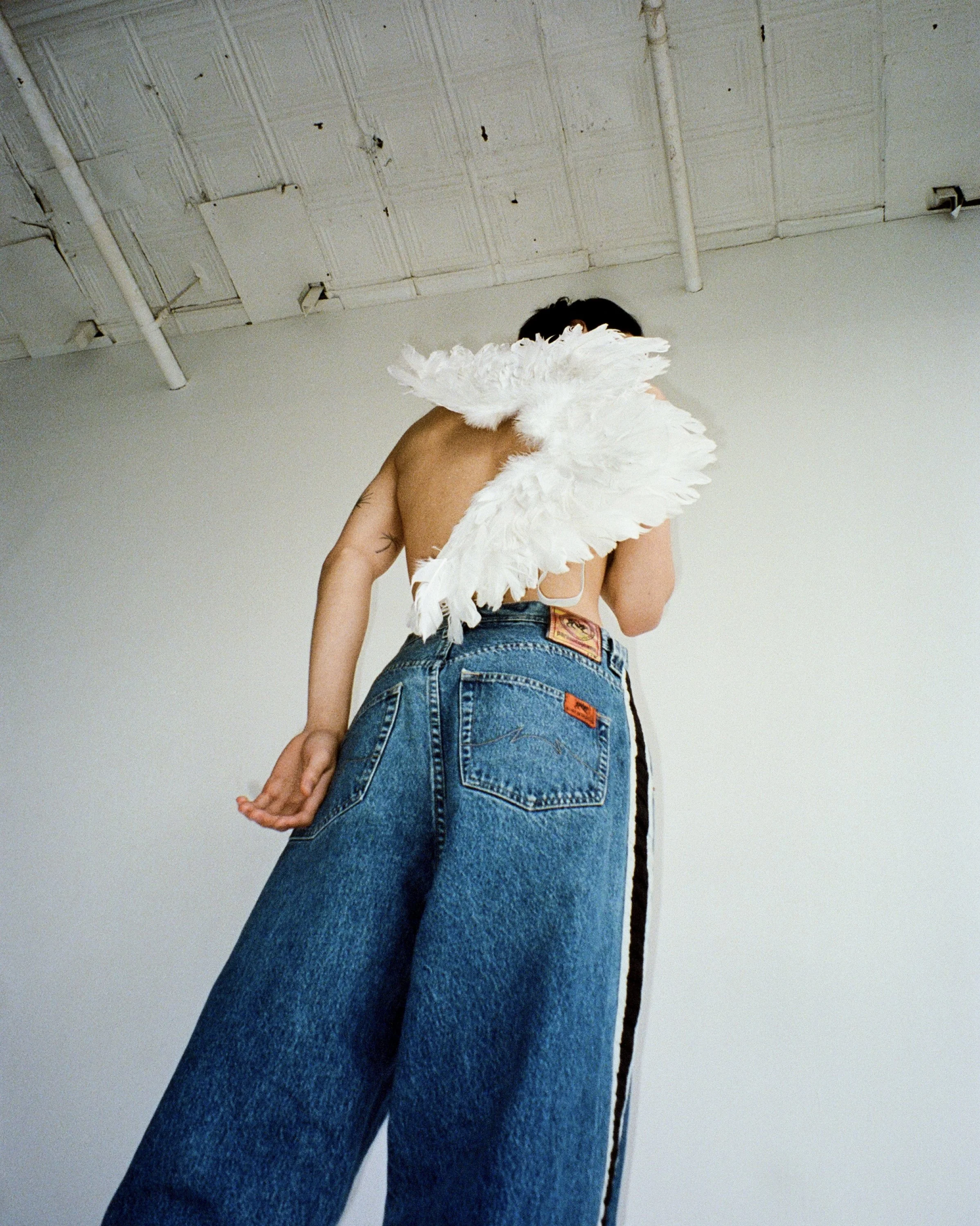 A man facing the opposite way wearing jeans and holding a pair of angel wings