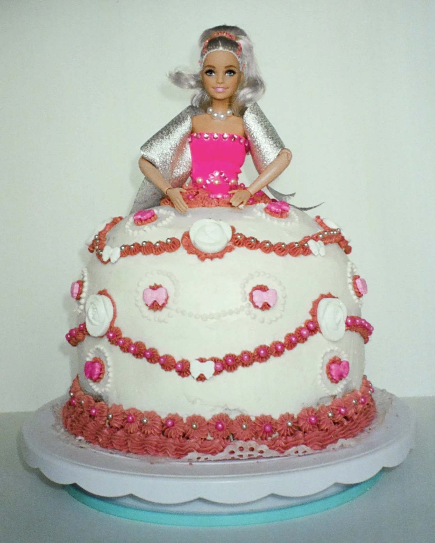 A close up photo of a Barbie cake with a pink dress and decorations.