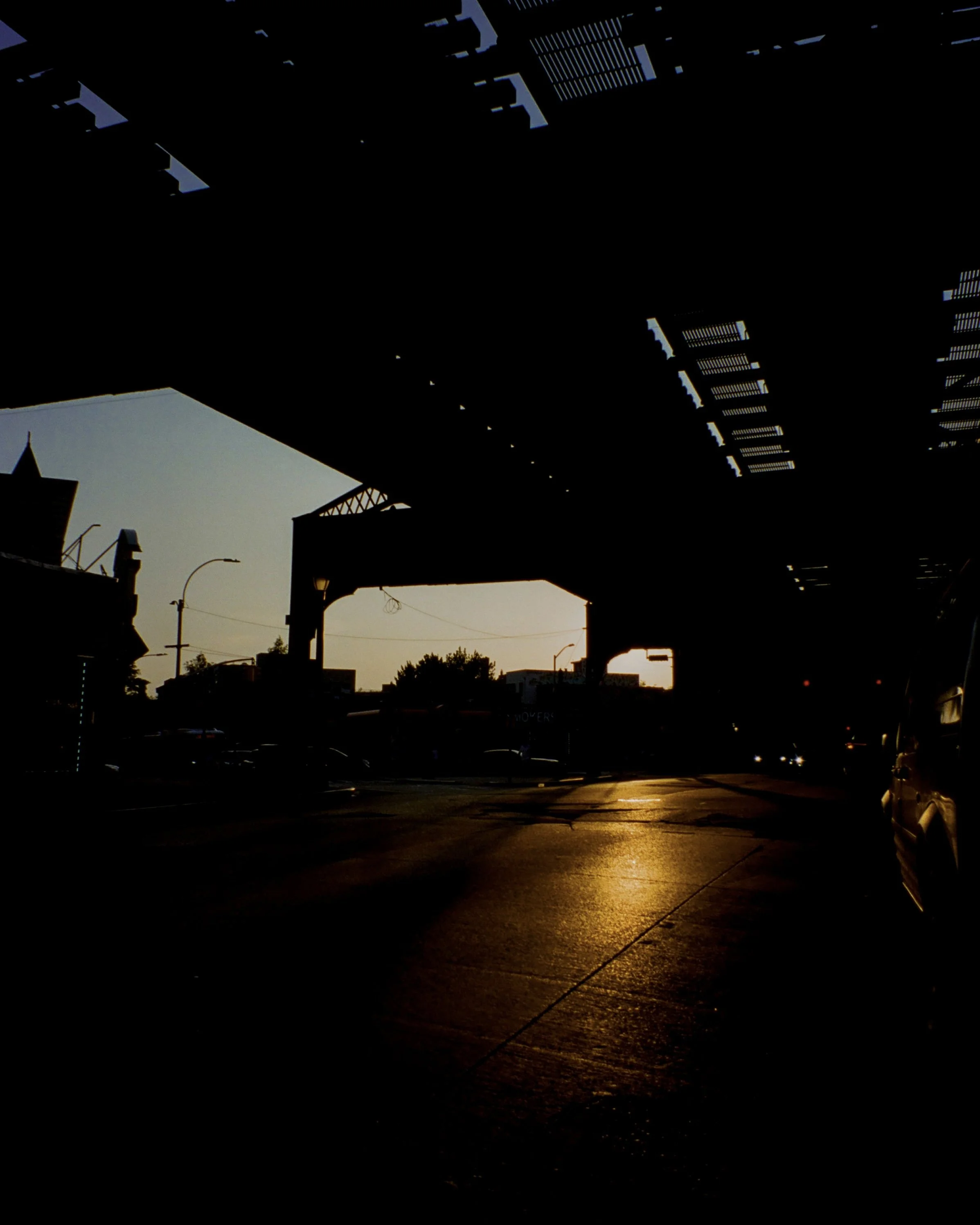 Photo of the sunset reflecting on an asphalt road with subway tracks above.