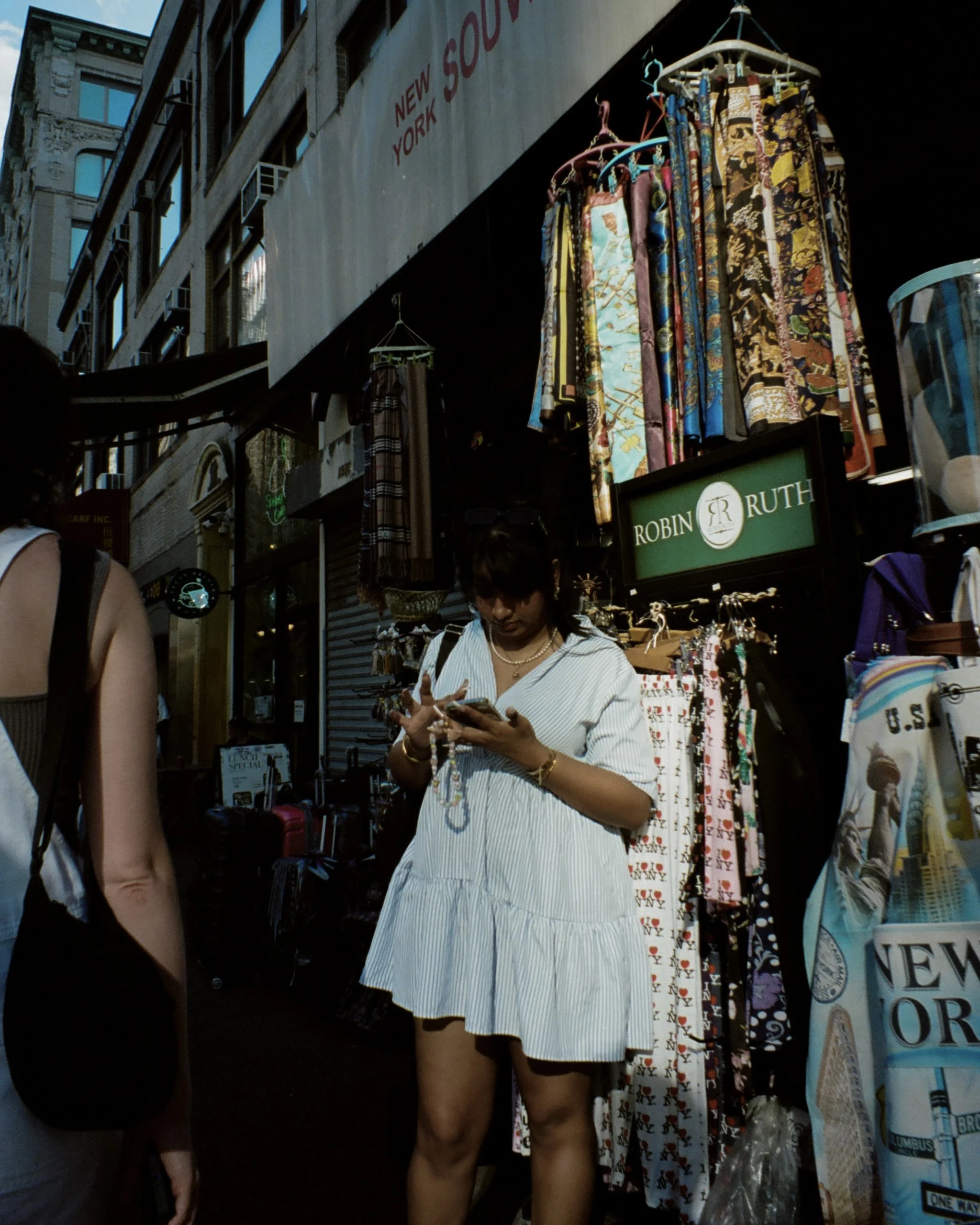 Image of a woman on her phone lit by ambient sunlight standing in front of a tourist store on Canal St in New York City