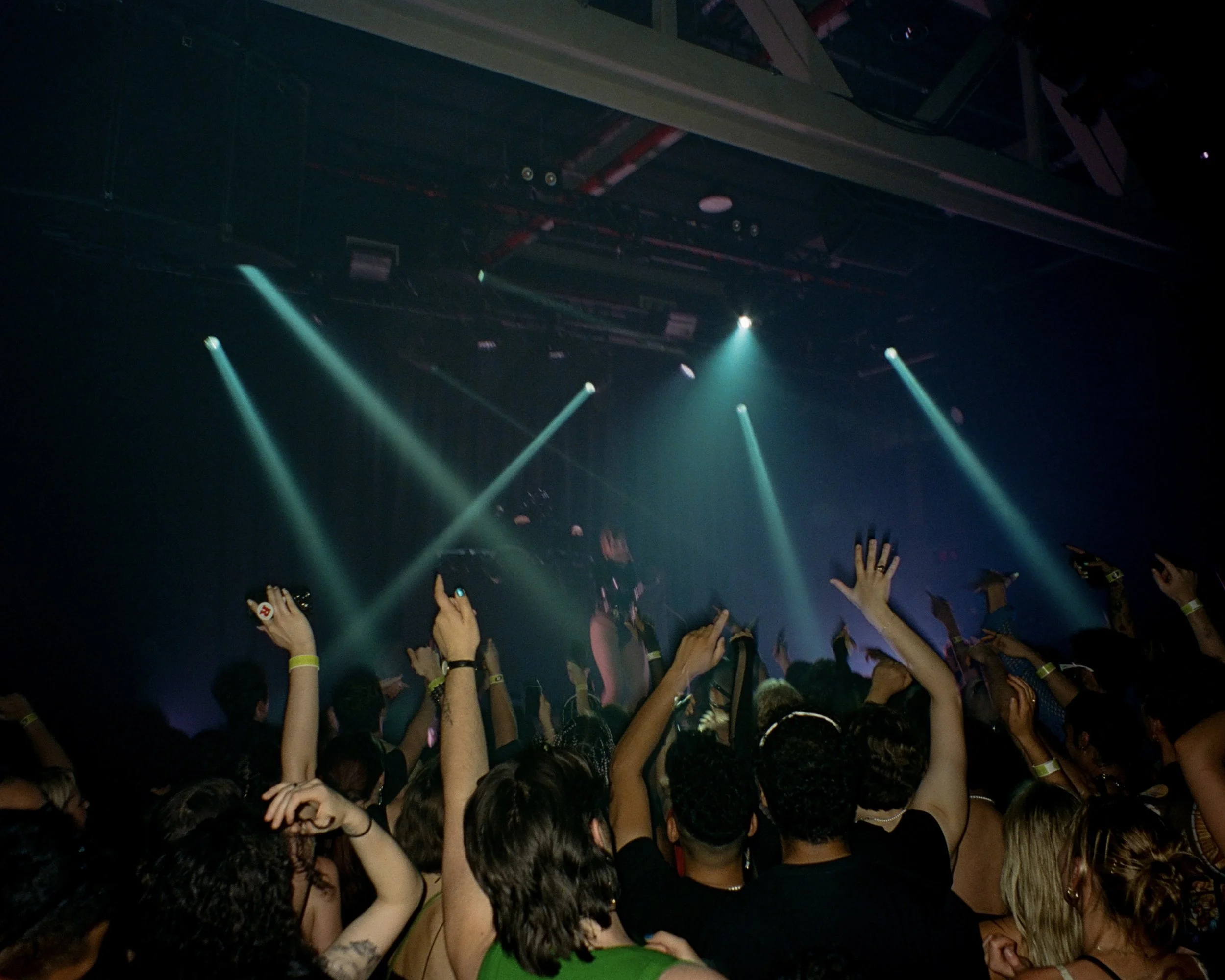 Photo of concert goers with their hands in the air illuminated by stage lights