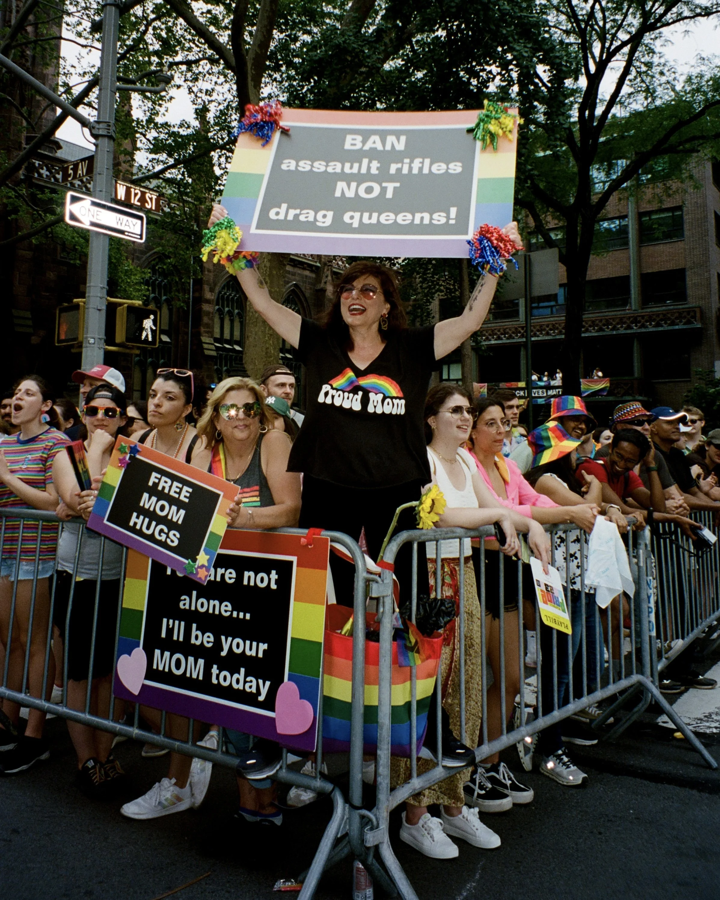 A photo of a woman holding a sign up at a pride parade that reads "BAN assault rifles NOT drag queens!"
