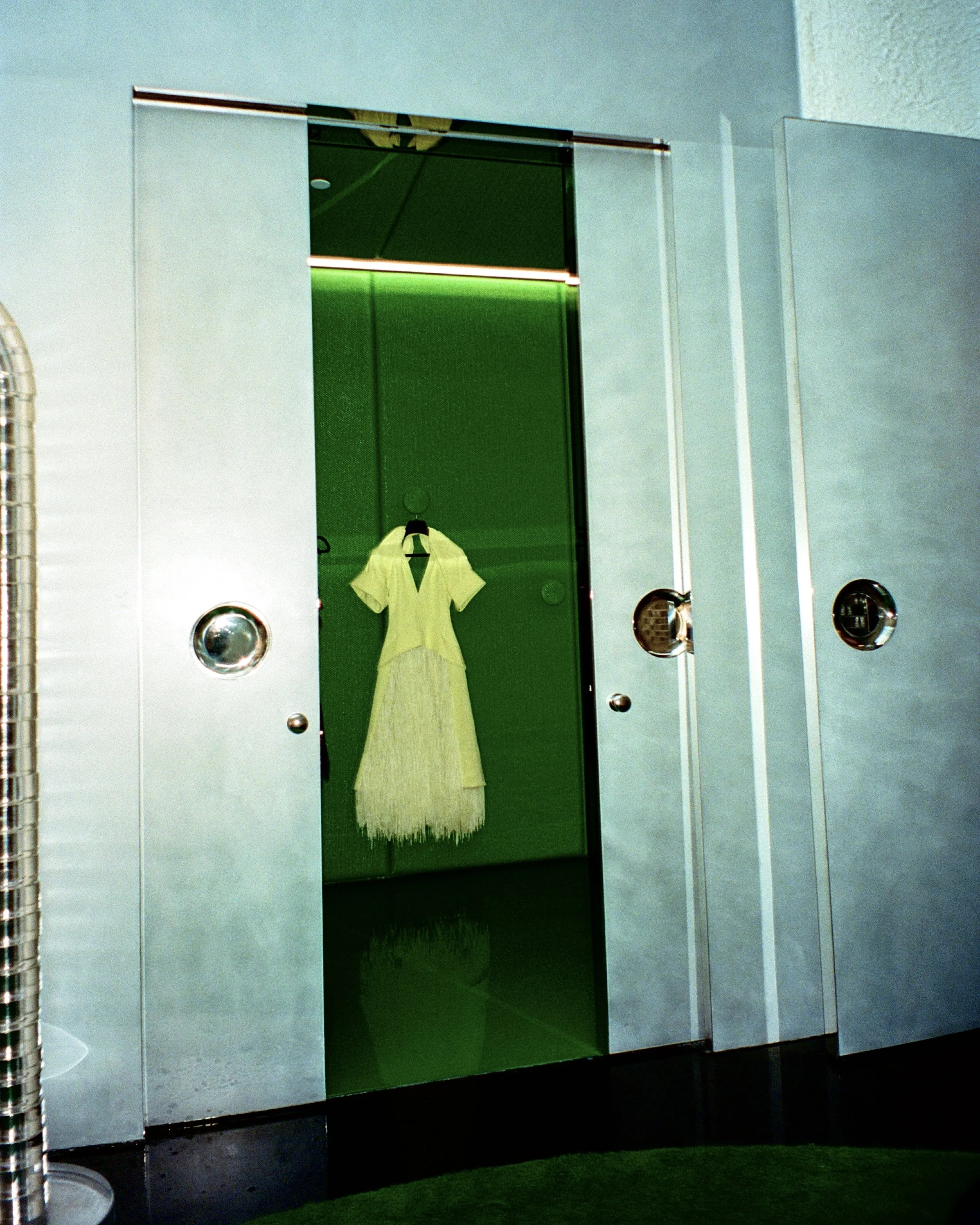 A white dress with leather fringe in a green fitting room